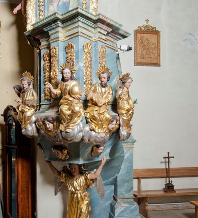 Zdjęcie nr 4: Ambona przyścienna, stojąca, z wejściem w postaci schodów z balustradą od strony prezbiterium. Kosz na planie ściętego z dwóch stron kwadratu, ustawiony pod kątem względem zaplecka, na profilowanym cokole, z podwieszonym u spodu zwężającym się w dół elementem podtrzymywanym przez figurę anioła. Dwie frontowe ścianki podzielone po środku pilastrami dźwigającymi pełne belkowanie o silnie wysuniętym gzymsie stanowiącym parapet kosza. Trzony pilastrów oraz pola pomiędzy nimi dekorowane są roślinnymi zwisami z muszlami. Na cokole kosza znajdują się siedzące na obłokach figury czterech ewangelistów z otwartymi księgami oraz na froncie figura Chrystusa trzymającego kulę. Podwieszony element pomiędzy siedzącymi figurami dekorowany jest obłokami i uskrzydlonymi główkami anielskimi. Balustrada schodów ozdobiona ornamentem roślinnym, zakończona półfilarem, na którym stoi figurka św. Jana Nepomucena. Zaplecek wąski, w formie stojącego prostokąta, z płyciną w polu ujętą profilowaną ramą w formie stojącego prostokąta zamkniętego łukiem segmentowym nadwieszonym z obrazem Chrystusa Dobrego Pasterza. Płycina flankowana rzędami kampanul, zwieńczona obłokiem z uskrzydloną główką anielską. Zaplecek z uszami z karbowanej wstęgi przeplatanej akantem, zwieńczony dwiema wolutami zwróconymi na zewnątrz. Całość zakończona ustawioną ukośnie glorią promienistą z gołębicą Ducha Świętego pośrodku. Struktura polichromowana na sposób imitujący błękitno-biało-różowy marmur. Dekoracja rzeźbiarska i ornamentalna pozłacana i posrebrzana, partie anatomiczne figur polichromowane naturalistycznie. 
