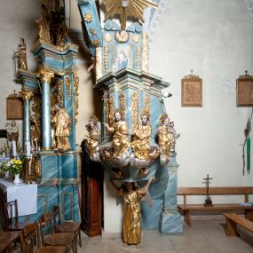 Zdjęcie nr 1: Ambona przyścienna, stojąca, z wejściem w postaci schodów z balustradą od strony prezbiterium. Kosz na planie ściętego z dwóch stron kwadratu, ustawiony pod kątem względem zaplecka, na profilowanym cokole, z podwieszonym u spodu zwężającym się w dół elementem podtrzymywanym przez figurę anioła. Dwie frontowe ścianki podzielone po środku pilastrami dźwigającymi pełne belkowanie o silnie wysuniętym gzymsie stanowiącym parapet kosza. Trzony pilastrów oraz pola pomiędzy nimi dekorowane są roślinnymi zwisami z muszlami. Na cokole kosza znajdują się siedzące na obłokach figury czterech ewangelistów z otwartymi księgami oraz na froncie figura Chrystusa trzymającego kulę. Podwieszony element pomiędzy siedzącymi figurami dekorowany jest obłokami i uskrzydlonymi główkami anielskimi. Balustrada schodów ozdobiona ornamentem roślinnym, zakończona półfilarem, na którym stoi figurka św. Jana Nepomucena. Zaplecek wąski, w formie stojącego prostokąta, z płyciną w polu ujętą profilowaną ramą w formie stojącego prostokąta zamkniętego łukiem segmentowym nadwieszonym z obrazem Chrystusa Dobrego Pasterza. Płycina flankowana rzędami kampanul, zwieńczona obłokiem z uskrzydloną główką anielską. Zaplecek z uszami z karbowanej wstęgi przeplatanej akantem, zwieńczony dwiema wolutami zwróconymi na zewnątrz. Całość zakończona ustawioną ukośnie glorią promienistą z gołębicą Ducha Świętego pośrodku. Struktura polichromowana na sposób imitujący błękitno-biało-różowy marmur. Dekoracja rzeźbiarska i ornamentalna pozłacana i posrebrzana, partie anatomiczne figur polichromowane naturalistycznie. 
