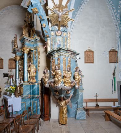 Zdjęcie nr 8: Ambona przyścienna, stojąca, z wejściem w postaci schodów z balustradą od strony prezbiterium. Kosz na planie ściętego z dwóch stron kwadratu, ustawiony pod kątem względem zaplecka, na profilowanym cokole, z podwieszonym u spodu zwężającym się w dół elementem podtrzymywanym przez figurę anioła. Dwie frontowe ścianki podzielone po środku pilastrami dźwigającymi pełne belkowanie o silnie wysuniętym gzymsie stanowiącym parapet kosza. Trzony pilastrów oraz pola pomiędzy nimi dekorowane są roślinnymi zwisami z muszlami. Na cokole kosza znajdują się siedzące na obłokach figury czterech ewangelistów z otwartymi księgami oraz na froncie figura Chrystusa trzymającego kulę. Podwieszony element pomiędzy siedzącymi figurami dekorowany jest obłokami i uskrzydlonymi główkami anielskimi. Balustrada schodów ozdobiona ornamentem roślinnym, zakończona półfilarem, na którym stoi figurka św. Jana Nepomucena. Zaplecek wąski, w formie stojącego prostokąta, z płyciną w polu ujętą profilowaną ramą w formie stojącego prostokąta zamkniętego łukiem segmentowym nadwieszonym z obrazem Chrystusa Dobrego Pasterza. Płycina flankowana rzędami kampanul, zwieńczona obłokiem z uskrzydloną główką anielską. Zaplecek z uszami z karbowanej wstęgi przeplatanej akantem, zwieńczony dwiema wolutami zwróconymi na zewnątrz. Całość zakończona ustawioną ukośnie glorią promienistą z gołębicą Ducha Świętego pośrodku. Struktura polichromowana na sposób imitujący błękitno-biało-różowy marmur. Dekoracja rzeźbiarska i ornamentalna pozłacana i posrebrzana, partie anatomiczne figur polichromowane naturalistycznie. 