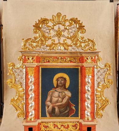 Zdjęcie nr 3: Feretron architektoniczny, ustawiony na cokole z wyodrębnionymi prostopadłościanami, w których znajdują się otwory na drążki, ujęty profilowanym gzymsem, w partii środkowej z dwóch stron dekorowany akantem. Rama w formie stojącego prostokąta, flankowana pilastrami oraz półkolumnami o skręconych trzonach, dźwigającymi belkowanie wyłamane na ich osi. Fryz zdobiony akantem. Feretron ujęty ażurowymi uszami utworzonymi z rocaille&#039;u i kratki; zwieńczony szczytem złożonym z rocaille&#039;u, wypełnionego ażurową kratką, z motywem sześcioramiennej gwiazdy w centrum na awersie oraz gorejącego serca na rewersie. Pole obrazowe w formie stojącego prostokąta. 
Na awersie przedstawienie Marki Boskiej z Dzieciątkiem. Maria ukazana w półpostaci, frontalnie, lewą ręką przytrzymuje Dzieciątko, w prawej, ugiętej trzyma trzy strzały. Twarz ma owalną, o regularnych rysach i ciemnej karnacji, małych oczach, krótkim nosie i niewielkich ustach. Ubrana jest w różową suknię, ze złoconą lamówką oraz jasnoniebieski, wzorzysty płaszcz, z czerwoną podszewką i złoconą lamówką, narzucony na głowę i ramiona. Na głowie ma koronę zamkniętą, wokół niej nimb i glorię. Dzieciątko ukazane w pozycji siedzącej, zwrócone w trzech czwartych w lewo, prawą rękę unosi w geście błogosławieństwa, lewą przytrzymuje na kolanach księgę. Twarz ma okrągłą, o ciemnej karnacji, małych oczach, krótkim nosie i pełnych ustach, okoloną krótkimi, ciemnobrązowymi włosami. Na głowie ma koronę zamkniętą, wokół niej nimb i glorię. Ubrane jest w czerwoną tunikę, ze złoconymi lamówkami. Postacie ukazane na jednolitym, niebieskim tle. 
Na rewersie przedstawienie Chrystusa w typie Ecce Homo, ukazanego do bioder, zwróconego w trzech czwartych w lewo, z uniesioną głową oraz ugiętymi i skrzyżowanymi z przodu rękami, przewiązanymi w nadgarstkach powrozem. Chrystus ma szczupłą, kwadratową twarz, o dużych oczach skierowanych w górę, krótkim nosie i pełnych, otwartych ustach z widocznymi zębami; okoloną krótką, jasną brodą oraz brązowymi włosami opadającymi na ramiona. Na głowie ma koronę cierniową, wokół niej złocony nimb. Przez biodra ma przewiązane obficie drapowane, białe perizonium, na ramiona ma narzucony srebrzysty płaszcz, z czerwoną podszewką i złoconą lamówką, zawiązany pod szyją niebieską wstęgą. Tors nagi, o lekko zarysowanej muskulaturze, bladej karnacji, z  zaznaczonymi, licznymi śladami męki. Chrystus ukazany na jednolitym, niebieskim tle. 