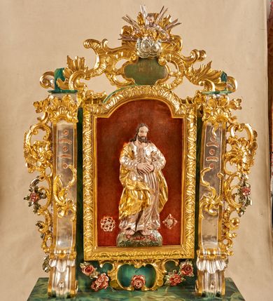 Zdjęcie nr 2: Podstawa na planie wydłużonego prostokąta, obwiedziona gzymsem, wyłamana w narożach, z otworami na drążki, dekorowana rozetami. Na niej zamocowana rama w formie zbliżonej do stojącego prostokąta, flankowana pilastrami ustawionymi na rocaille&#039;owych konsolach, o trzonach w formie przeszklonych gablot na relikwie na awersie oraz z rocaille&#039;m na rewersie oraz o rocaille&#039;owych kapitelach, dźwigających stylizowane imposty zakończone wolutami. Po bokach pilastrów rocaille z kwiatami. Rama zwieńczona szczytem utworzonym z rokokowego kartusza i anthemionu, ujętego rocaille&#039;m na awersie i rokokowego kartusza z nieczytelnym napisem „HR[...] / MI[...]” oraz niewielką półpostacią Boga Ojca na rewersie. U dołu, po obu stronach dekorowana rokokowym kartuszem flankowanym zwisami kwiatowymi. Pole obrazowe w formie stojącego prostokąta zamkniętego łukiem odcinkowym nadwieszonym, ujęte ramą dekorowaną motywem roślinnym. Na awersie obraz przedstawiający apoteozę św. Jana Nepomucena. W centrum postać świętego unoszącego się na obłokach, w pozycji siedzącej, zwróconego w trzech czwartych w lewo. Prawą rękę wyciąga przed siebie, lewą przytrzymuje na kolanach księgę i krucyfiks na ramieniu. Twarz ma owalną, o wysokim czole, dużych oczach skierowanych w górę, małym nosie i ustach, okoloną krótkimi, brązowymi włosami i brodą. Ubrany jest w czarną sutannę, białą komże lamowaną koronką oraz szarą almucję. Przed świętym na obłokach leży liść palmy i czarny biret, obok niego unosi się putto trzymając mu nad głową gwieździstą aureolę, pod nim putto trzyma kłódkę, a wokół niego unoszą się trzy uskrzydlone główki anielskie. Święty ukazany na tle obłoków. W dolnej części obrazu przedstawiony jest most Karola w Pradze na rzece Wełtawie, pośród pejzażu. Na rewersie płaskorzeźbione przedstawienie Chrystusa stojącego na globie dekorowanym kwiatami, ukazanego frontalnie, ze złożonymi z przodu dłońmi. Twarz ma pociągłą, o wysokim czole, dużych, migdałowatych oczach, dużym nosie i ustach, okoloną kręconymi włosami i brodą. Ubrany w srebrzoną tunikę oraz złocony płaszcz przewiązany przez prawe ramię i opadający po bokach postaci. Chrystusa w dolnej części przedstawienia flankują dwie rozety. Postać ukazana na laserowanym i cieniowanym, czerwonym tle. 





