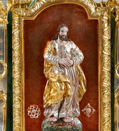 Zdjęcie nr 4: Podstawa na planie wydłużonego prostokąta, obwiedziona gzymsem, wyłamana w narożach, z otworami na drążki, dekorowana rozetami. Na niej zamocowana rama w formie zbliżonej do stojącego prostokąta, flankowana pilastrami ustawionymi na rocaille&#039;owych konsolach, o trzonach w formie przeszklonych gablot na relikwie na awersie oraz z rocaille&#039;m na rewersie oraz o rocaille&#039;owych kapitelach, dźwigających stylizowane imposty zakończone wolutami. Po bokach pilastrów rocaille z kwiatami. Rama zwieńczona szczytem utworzonym z rokokowego kartusza i anthemionu, ujętego rocaille&#039;m na awersie i rokokowego kartusza z nieczytelnym napisem „HR[...] / MI[...]” oraz niewielką półpostacią Boga Ojca na rewersie. U dołu, po obu stronach dekorowana rokokowym kartuszem flankowanym zwisami kwiatowymi. Pole obrazowe w formie stojącego prostokąta zamkniętego łukiem odcinkowym nadwieszonym, ujęte ramą dekorowaną motywem roślinnym. Na awersie obraz przedstawiający apoteozę św. Jana Nepomucena. W centrum postać świętego unoszącego się na obłokach, w pozycji siedzącej, zwróconego w trzech czwartych w lewo. Prawą rękę wyciąga przed siebie, lewą przytrzymuje na kolanach księgę i krucyfiks na ramieniu. Twarz ma owalną, o wysokim czole, dużych oczach skierowanych w górę, małym nosie i ustach, okoloną krótkimi, brązowymi włosami i brodą. Ubrany jest w czarną sutannę, białą komże lamowaną koronką oraz szarą almucję. Przed świętym na obłokach leży liść palmy i czarny biret, obok niego unosi się putto trzymając mu nad głową gwieździstą aureolę, pod nim putto trzyma kłódkę, a wokół niego unoszą się trzy uskrzydlone główki anielskie. Święty ukazany na tle obłoków. W dolnej części obrazu przedstawiony jest most Karola w Pradze na rzece Wełtawie, pośród pejzażu. Na rewersie płaskorzeźbione przedstawienie Chrystusa stojącego na globie dekorowanym kwiatami, ukazanego frontalnie, ze złożonymi z przodu dłońmi. Twarz ma pociągłą, o wysokim czole, dużych, migdałowatych oczach, dużym nosie i ustach, okoloną kręconymi włosami i brodą. Ubrany w srebrzoną tunikę oraz złocony płaszcz przewiązany przez prawe ramię i opadający po bokach postaci. Chrystusa w dolnej części przedstawienia flankują dwie rozety. Postać ukazana na laserowanym i cieniowanym, czerwonym tle. 





