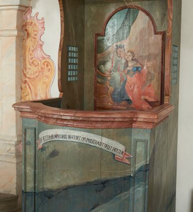 Zdjęcie nr 4: Konfesjonał na rzucie prostokąta zamkniętego od przodu łukiem segmentowym nadwieszonym, ustawiony na profilowanym cokole. Wybrzuszone przedpiersie ujęte lizenami z płycinami, zamknięte profilowanym gzymsem, u góry głównego pola przedpiersia namalowana banderola z napisem „NON MULTUM AB IMPECCABILI DISCEDIT, QVI PECCATUM UT DECET FATETUR. Aristoteles.”. Zaplecek z płyciną w polu w formie stojącego prostokąta zamkniętego łukiem półkolistym nadwieszonym, o wklęsłym dolnym odcinku. W polu malowana scena spowiedzi królowej u św. Jana Nepomucena. W lewej części sceny święty ukazany w pozycji siedzącej, na fotelu, prawą ręką wspiera się na podłokietniku, lewą podpiera głowę. Ubrany jest w sutannę, komżę, na ramionach ma stułę, a na głowie biret. W prawej części sceny ukazana jest klęcząca królowa, z lewą ręką złożoną na piersi, prawą wyciągniętą do góry. Ubrana jest w długą suknię, dołem czerwoną, w górnej części niebieską, przepasaną w talii, jasnobrązowy płaszcz, na głowie ma koronę otwartą. Scena ukazana jest we wnętrzu, w górnej części, po lewej, podwieszona zielona kurtyna. W dolnym podłuczu płyciny napis: „Solve Vincula Colli tui Captiva Filia / Sion. Ecclesia St 52”. 
Zaplecek ujęty ściankami bocznymi, w dolnej połowie szerokimi, zamkniętymi profilowanym gzymsem stanowiącym kontynuację gzymsu wieńczącego przedpiersie, z prostokątnymi drzwiczkami na zawiasach z lewej strony. W górnej połowie ścianki są węższe, o fantazyjnym wykroju, zakończone wolutą, z prostokątnymi prześwitami wypełnionymi kratką. Całość zwieńczona jest baldachimem na tym samym rzucie co korpus, ujętym z trzech stron belkowaniem. W partii frontowej fryzu malowana banderola z napisem: „PECCAVIMUS, INIQVITATEM FECIMUS, IMPIE EGIMUS. Danielis 9.”. Na podniebieniu baldachimu płycina w kształcie kwadratu wpisanego w czteroliść. W polu malowane przedstawienie aniołka w locie, który w prawej ręce trzyma język oraz liść palmy, w lewej zaś wieniec laurowy i kłódkę. Struktura konfesjonału polichromowana w sposób imitujący marmur w kolorze zielono-niebieskim, cokół, gzymsy i profile polichromowana w sposób imitujący marmur w kolorze jasnoczerwonym. 
