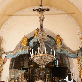 Zdjęcie nr 1: Belka tęczowa złożona z trzech elementów – dwóch bocznych w formie falistych i wyłamanych fragmentów belkowania, na których opiera się trzeci element w kształcie łuku kotarowego z uskokiem na ćwierćkolistych konsolach. Belka dekorowana rocaille'm i rozetami, podtrzymywana przez dwie pary puttów.   Na zwieńczeniu łuku krzyż z figurą Chrystusa przymocowany do ściany tęczowej. Jezus ukazany jako umarły, przybity do krzyża trzema gwoździami. Jego ciało jest w lekkim zwisie, o szeroko rozłożonych ramionach, z głową opadająca bezwładnie na prawy bark, stopy skrzyżowane w układzie prawa na lewą. Chrystus ma podłużną twarz, o zamkniętych oczach, dużym nosie i szeroko otwartych ustach z widocznymi zębami; okoloną kręconymi i brązowymi włosami i brodą. Na głowie ma szeroką, ciemnozieloną koronę cierniową. Jego ciało jest silnie umięśnione, z podkreślonymi żebrami i mostkiem oraz zaznaczonymi śladami męki. Przez biodra ma przewiązane krótkie, srebrzone perizonium, silnie drapowane, ze zwisem tkaniny na lewym boku. Krzyż ciemnobrązowy, o prostym zakończeniu ramion, pionowa bela zwieńczona białą banderolą z napisem „INRI”. Pod krzyżem klęczy św. Maria Magdalena, zwrócona profilem w lewo, z pochyloną głową oraz wyciągniętymi do przodu rękami. Twarz ma owalna, o pełnych policzkach, małych oczach i nosie oraz otwartych ustach, okoloną długimi, falistymi włosami, opadającymi na plecy. Ubrana jest w złoconą suknię o szerokich, podwiniętych rękawach oraz złocony płaszcz zawinięty wokół pasa i nóg. Po prawej stronie krzyża stoi Matka Boska ukazana frontalnie, z uniesioną głową, lewą rękę kładzie na piersi, prawą wyciąga w bok. Twarz ma owalną, o oczach uniesionych w górę, małym nosie i ustach. Ubrana jest w złoconą suknię i płaszcz, na głowie ma złocony welon. Po lewej stronie krzyża stoi św. Jan Ewangelista, ukazany frontalnie, z uniesioną głową, prawą rękę kładzie na piersi, lewą wyciąga w bok. Twarz ma owalną, o oczach uniesionych w górę, małym nosie i ustach, okoloną krótkimi, brązowymi włosami. Ubrany jest w złoconą tunikę i płaszcz, zawinięty wokół bioder. Polichromia ciał postaci naturalistyczna. 



