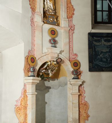 Zdjęcie nr 2: W narożach ośmiobocznej kaplicy Matki Boskiej Karmelitańskiej znajduje się osiem nisz z siedziskami, ujętych parami pilastrów podtrzymujących archiwoltę z kluczem, pod ich łukami podwieszone figury proroków, na kluczu i głowicach pilastrów ustawione wazony ze słonecznikami. Nad nimi, na wysokim cokole mniejsze, analogiczne nisze z figurami świętych stojącymi na cokołach. Architektoniczna konstrukcja ujęta malowanym rocaille'm. 
Figury proroków podwieszone w dolnych niszach mają ugięte nogi i rozłożone na boki ręce, w których trzymają banderole. Przedstawieni są jako starcy z długimi brodami lub jako dojrzali mężczyźni z krótkimi. Figury Dawida i Salomona ukazane są w strojach królewskich, z koronami na głowach. Rzeźba Balaama przedstawiona jest w tunice i płaszczu, z głową oślicy przy nodze. Melchizedek jest w stroju kapłańskim, z albą, komżą i stułą. Elizeusz ubrany jest w tunikę i płaszcz, na głowie ma turban, a przy nodze głowę wołu. Pozostałe figury pozbawione atrybutów, ukazane są w tunikach i płaszczach lub szatach spodnich i wierzchnich. 
Figury świętych z górnego rzędu nisz ustawione są na cokołach i na rzeźbionych podstawach w formie obłoków, ujętych spływami wolutowymi, dekorowanymi rozetami z przodu. Rzeźby ukazane są frontalnie lub zwrócone trzy czwarte w bok, ręce mają rozłożone na boki lub jedną złożona na piersi. Ukazani są jako dojrzali mężczyźni z krótkimi kręconymi brodami i kręconymi włosami opadającymi na ramiona. Ubrani są w tuniki przylegające do ciała oraz płaszcze. Wyłącznie część figur posiada atrybuty. Święty Juda Tadeusz ukazany jest z pałką, św. Bartłomiej z płaszczem z ludzką twarzą (skóra), św. Szymon z piłą, św. Filip z kamieniami w dłoni, św. Maciej lub św. Tomasz z włócznią oraz św. Jakub Mniejszy z rozetą i księgą.  
Figury polichromowane są naturalistycznie w partiach ciała, szaty i atrybuty są złocone, srebrzone, laserowane lub polichromowane. 
