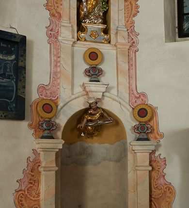 Zdjęcie nr 4: W narożach ośmiobocznej kaplicy Matki Boskiej Karmelitańskiej znajduje się osiem nisz z siedziskami, ujętych parami pilastrów podtrzymujących archiwoltę z kluczem, pod ich łukami podwieszone figury proroków, na kluczu i głowicach pilastrów ustawione wazony ze słonecznikami. Nad nimi, na wysokim cokole mniejsze, analogiczne nisze z figurami świętych stojącymi na cokołach. Architektoniczna konstrukcja ujęta malowanym rocaille'm. 
Figury proroków podwieszone w dolnych niszach mają ugięte nogi i rozłożone na boki ręce, w których trzymają banderole. Przedstawieni są jako starcy z długimi brodami lub jako dojrzali mężczyźni z krótkimi. Figury Dawida i Salomona ukazane są w strojach królewskich, z koronami na głowach. Rzeźba Balaama przedstawiona jest w tunice i płaszczu, z głową oślicy przy nodze. Melchizedek jest w stroju kapłańskim, z albą, komżą i stułą. Elizeusz ubrany jest w tunikę i płaszcz, na głowie ma turban, a przy nodze głowę wołu. Pozostałe figury pozbawione atrybutów, ukazane są w tunikach i płaszczach lub szatach spodnich i wierzchnich. 
Figury świętych z górnego rzędu nisz ustawione są na cokołach i na rzeźbionych podstawach w formie obłoków, ujętych spływami wolutowymi, dekorowanymi rozetami z przodu. Rzeźby ukazane są frontalnie lub zwrócone trzy czwarte w bok, ręce mają rozłożone na boki lub jedną złożona na piersi. Ukazani są jako dojrzali mężczyźni z krótkimi kręconymi brodami i kręconymi włosami opadającymi na ramiona. Ubrani są w tuniki przylegające do ciała oraz płaszcze. Wyłącznie część figur posiada atrybuty. Święty Juda Tadeusz ukazany jest z pałką, św. Bartłomiej z płaszczem z ludzką twarzą (skóra), św. Szymon z piłą, św. Filip z kamieniami w dłoni, św. Maciej lub św. Tomasz z włócznią oraz św. Jakub Mniejszy z rozetą i księgą.  
Figury polichromowane są naturalistycznie w partiach ciała, szaty i atrybuty są złocone, srebrzone, laserowane lub polichromowane. 
