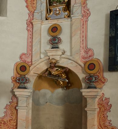 Zdjęcie nr 5: W narożach ośmiobocznej kaplicy Matki Boskiej Karmelitańskiej znajduje się osiem nisz z siedziskami, ujętych parami pilastrów podtrzymujących archiwoltę z kluczem, pod ich łukami podwieszone figury proroków, na kluczu i głowicach pilastrów ustawione wazony ze słonecznikami. Nad nimi, na wysokim cokole mniejsze, analogiczne nisze z figurami świętych stojącymi na cokołach. Architektoniczna konstrukcja ujęta malowanym rocaille&#039;m. 
Figury proroków podwieszone w dolnych niszach mają ugięte nogi i rozłożone na boki ręce, w których trzymają banderole. Przedstawieni są jako starcy z długimi brodami lub jako dojrzali mężczyźni z krótkimi. Figury Dawida i Salomona ukazane są w strojach królewskich, z koronami na głowach. Rzeźba Balaama przedstawiona jest w tunice i płaszczu, z głową oślicy przy nodze. Melchizedek jest w stroju kapłańskim, z albą, komżą i stułą. Elizeusz ubrany jest w tunikę i płaszcz, na głowie ma turban, a przy nodze głowę wołu. Pozostałe figury pozbawione atrybutów, ukazane są w tunikach i płaszczach lub szatach spodnich i wierzchnich. 
Figury świętych z górnego rzędu nisz ustawione są na cokołach i na rzeźbionych podstawach w formie obłoków, ujętych spływami wolutowymi, dekorowanymi rozetami z przodu. Rzeźby ukazane są frontalnie lub zwrócone trzy czwarte w bok, ręce mają rozłożone na boki lub jedną złożona na piersi. Ukazani są jako dojrzali mężczyźni z krótkimi kręconymi brodami i kręconymi włosami opadającymi na ramiona. Ubrani są w tuniki przylegające do ciała oraz płaszcze. Wyłącznie część figur posiada atrybuty. Święty Juda Tadeusz ukazany jest z pałką, św. Bartłomiej z płaszczem z ludzką twarzą (skóra), św. Szymon z piłą, św. Filip z kamieniami w dłoni, św. Maciej lub św. Tomasz z włócznią oraz św. Jakub Mniejszy z rozetą i księgą.  
Figury polichromowane są naturalistycznie w partiach ciała, szaty i atrybuty są złocone, srebrzone, laserowane lub polichromowane. 