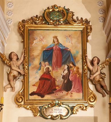 Zdjęcie nr 1: Obraz w formie stojącego prostokąta, ujęty profilowaną ramą, dekorowaną szczytem utworzonym z rocaille&#039;owego kartusza z monogramem Marii w polu, flankowanym rocaille&#039;m i kwiatami, podtrzymywanym w narożach konsolami. U dołu ramy podwieszenie utworzone z rocaille&#039;owego kartusza z napisem „S(ANTA) MARIA / ORA PRO NOBIS”, ujęte rocaille&#039;m i konsolami w narożach. Po bokach ramę trzymają nadlatujące putta. W centralnej części obrazu Matka Boska ukazana w pozycji stojącej pośród obłoków, z pochyloną głową i rozłożonymi na boki rękami podtrzymującymi płaszcz. Ubrana jest w różową suknię, przepasaną w talii, na ramionach ma obszerny, niebieski płaszcz, wokół głowy zawiązaną jasnobrązową chustę, na głowie koronę otwartą. W dolnej części kompozycji ukazane dwie grupy klęczących świętych, zwróconych do wewnątrz. Po lewej tronie św. Piotr. św. Stanisław i św. Stefan (?). Na pierwszym planie św. Stefan ukazany z profilu, z wyciągniętą w przód prawą ręką. Okolony jest krótką brodą i długimi, brązowymi włosami, ubrany w czerwony płaszcz królewski, ze złoconym wzorem, obszyty futrem. Przed nim na różowej poduszce z chwostami leży korona i jabłko królewskie. Obok niego św. Stanisław pozbawiony brody, w stroju biskupim, w żółtej kapie i infule oraz św. Piotr ukazany jako strzec, okolony siwymi włosami i brodą, w żółtym płaszczu. Po prawej stronie obrazu klęczą św. zakonnica, św. Katarzyna Aleksandryjska i św. Elżbieta Węgierska. Zakonnica ubrana jest w brązowy habit i welon oraz białą podwikę, prawą ręką przytrzymuje białą flagę, lewą wyciąga w bok. Obok niej klęczy św. Katarzyna z rekami złożonymi w geście modlitwy, o długich jasnych włosach. Ubrana jest w różowy płaszcz, na głowie ma koronę otwartą. Obok niej leży fragment koła. Za nimi postać św. Elżbiety, która podtrzymuje kwiaty róż. Ubrana jest w zielony płaszcz, na głowie ma czarny welon i koronę otwartą. Scena ukazana na tle jasnobłękitnego nieba wypełnionego żółto-brązowymi obłokami. W górnej części obrazu ukazane trzy putta. W dolnej części obrazu napis: „FUNDATORZY / MYSLIWIEC LUDWIK. IGLAR MACIEJ. GURCZYK PAWEŁ”. W prawym dolnym narożu obrazu sygnatura: „MAL(OWAŁ) KÛC ANTONI / 1932.”
