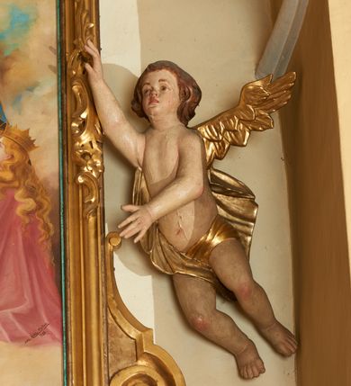 Zdjęcie nr 5: Obraz w formie stojącego prostokąta, ujęty profilowaną ramą, dekorowaną szczytem utworzonym z rocaille&#039;owego kartusza z monogramem Marii w polu, flankowanym rocaille&#039;m i kwiatami, podtrzymywanym w narożach konsolami. U dołu ramy podwieszenie utworzone z rocaille&#039;owego kartusza z napisem „S(ANTA) MARIA / ORA PRO NOBIS”, ujęte rocaille&#039;m i konsolami w narożach. Po bokach ramę trzymają nadlatujące putta. W centralnej części obrazu Matka Boska ukazana w pozycji stojącej pośród obłoków, z pochyloną głową i rozłożonymi na boki rękami podtrzymującymi płaszcz. Ubrana jest w różową suknię, przepasaną w talii, na ramionach ma obszerny, niebieski płaszcz, wokół głowy zawiązaną jasnobrązową chustę, na głowie koronę otwartą. W dolnej części kompozycji ukazane dwie grupy klęczących świętych, zwróconych do wewnątrz. Po lewej tronie św. Piotr. św. Stanisław i św. Stefan (?). Na pierwszym planie św. Stefan ukazany z profilu, z wyciągniętą w przód prawą ręką. Okolony jest krótką brodą i długimi, brązowymi włosami, ubrany w czerwony płaszcz królewski, ze złoconym wzorem, obszyty futrem. Przed nim na różowej poduszce z chwostami leży korona i jabłko królewskie. Obok niego św. Stanisław pozbawiony brody, w stroju biskupim, w żółtej kapie i infule oraz św. Piotr ukazany jako strzec, okolony siwymi włosami i brodą, w żółtym płaszczu. Po prawej stronie obrazu klęczą św. zakonnica, św. Katarzyna Aleksandryjska i św. Elżbieta Węgierska. Zakonnica ubrana jest w brązowy habit i welon oraz białą podwikę, prawą ręką przytrzymuje białą flagę, lewą wyciąga w bok. Obok niej klęczy św. Katarzyna z rekami złożonymi w geście modlitwy, o długich jasnych włosach. Ubrana jest w różowy płaszcz, na głowie ma koronę otwartą. Obok niej leży fragment koła. Za nimi postać św. Elżbiety, która podtrzymuje kwiaty róż. Ubrana jest w zielony płaszcz, na głowie ma czarny welon i koronę otwartą. Scena ukazana na tle jasnobłękitnego nieba wypełnionego żółto-brązowymi obłokami. W górnej części obrazu ukazane trzy putta. W dolnej części obrazu napis: „FUNDATORZY / MYSLIWIEC LUDWIK. IGLAR MACIEJ. GURCZYK PAWEŁ”. W prawym dolnym narożu obrazu sygnatura: „MAL(OWAŁ) KÛC ANTONI / 1932.”
