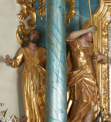 Zdjęcie nr 5: Ołtarz drewniany, prostopadłościenny z drewnianą mensą, w polu antepedium malowana na drewnie scena Zwiastowania (kopia obrazu Leonarda da Vinci). Na ołtarzu stoi tabliczka z kanonem w otoczeniu akantowych wolut tworzących podstawę dla pięciu lichtarzy utworzonych z ornamentu roślinnego. 
Nastawa architektoniczna, jednoosiowa, jednokondygnacyjna ze zwieńczeniem, ustawiona na dwustrefowym cokole, ujęta parą półfilarów i stojącą przed nimi parą kolumn dźwigających pełne belkowanie, przerwane nad polem środkowym. Na cokołach kolumn kanony w ornamentalnych ramach. Kolumny flankują od zewnątrz figury św. Tomasza (?) i św. Jana Nepomucena, od wewnątrz św. Michała Archanioła i św. Jerzego. W polu głównym obraz Matki Boskiej Szkaplerznej w formie stojącego prostokąta zamkniętego łukiem półkolistym nadwieszonym z uskokiem w profilowanej, dekorowanej ornamentem roślinnym ramie. Ponad nim kartusz ujęty ornamentem rocaille'owym i kratką regencyjną oraz uskrzydloną główką anielską flankowaną rocaille'ami. Zwieńczenie w formie leżącego prostokąta ujętego spływami wolutowymi dekorowanymi rocaille'ami, zamkniętego fragmentem falującego gzymsu z monogramem Marii w otoku z obłoków w glorii promienistej. W polu rzeźbiarskie przedstawienie św. Katarzyny Aleksandryjskiej flankowanej obłokami i wiązkami promieni oraz parą puttów. Na belkowaniu figury św. Rozalii i św. Calamindy. Ołtarz ujęty uszami utworzonymi z ornamentu rocaille'owego i kratki regencyjnej. Struktura polichromowana w sposób naśladujący marmoryzację w kolorze niebiesko-białym, profile i ornamentyka pozłacane.