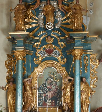 Zdjęcie nr 13: Ołtarz drewniany, prostopadłościenny z drewnianą mensą, w polu antepedium malowana na drewnie scena Zwiastowania (kopia obrazu Leonarda da Vinci). Na ołtarzu stoi tabliczka z kanonem w otoczeniu akantowych wolut tworzących podstawę dla pięciu lichtarzy utworzonych z ornamentu roślinnego. 
Nastawa architektoniczna, jednoosiowa, jednokondygnacyjna ze zwieńczeniem, ustawiona na dwustrefowym cokole, ujęta parą półfilarów i stojącą przed nimi parą kolumn dźwigających pełne belkowanie, przerwane nad polem środkowym. Na cokołach kolumn kanony w ornamentalnych ramach. Kolumny flankują od zewnątrz figury św. Tomasza (?) i św. Jana Nepomucena, od wewnątrz św. Michała Archanioła i św. Jerzego. W polu głównym obraz Matki Boskiej Szkaplerznej w formie stojącego prostokąta zamkniętego łukiem półkolistym nadwieszonym z uskokiem w profilowanej, dekorowanej ornamentem roślinnym ramie. Ponad nim kartusz ujęty ornamentem rocaille'owym i kratką regencyjną oraz uskrzydloną główką anielską flankowaną rocaille'ami. Zwieńczenie w formie leżącego prostokąta ujętego spływami wolutowymi dekorowanymi rocaille'ami, zamkniętego fragmentem falującego gzymsu z monogramem Marii w otoku z obłoków w glorii promienistej. W polu rzeźbiarskie przedstawienie św. Katarzyny Aleksandryjskiej flankowanej obłokami i wiązkami promieni oraz parą puttów. Na belkowaniu figury św. Rozalii i św. Calamindy. Ołtarz ujęty uszami utworzonymi z ornamentu rocaille'owego i kratki regencyjnej. Struktura polichromowana w sposób naśladujący marmoryzację w kolorze niebiesko-białym, profile i ornamentyka pozłacane.