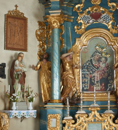 Zdjęcie nr 17: Ołtarz drewniany, prostopadłościenny z drewnianą mensą, w polu antepedium malowana na drewnie scena Zwiastowania (kopia obrazu Leonarda da Vinci). Na ołtarzu stoi tabliczka z kanonem w otoczeniu akantowych wolut tworzących podstawę dla pięciu lichtarzy utworzonych z ornamentu roślinnego. 
Nastawa architektoniczna, jednoosiowa, jednokondygnacyjna ze zwieńczeniem, ustawiona na dwustrefowym cokole, ujęta parą półfilarów i stojącą przed nimi parą kolumn dźwigających pełne belkowanie, przerwane nad polem środkowym. Na cokołach kolumn kanony w ornamentalnych ramach. Kolumny flankują od zewnątrz figury św. Tomasza (?) i św. Jana Nepomucena, od wewnątrz św. Michała Archanioła i św. Jerzego. W polu głównym obraz Matki Boskiej Szkaplerznej w formie stojącego prostokąta zamkniętego łukiem półkolistym nadwieszonym z uskokiem w profilowanej, dekorowanej ornamentem roślinnym ramie. Ponad nim kartusz ujęty ornamentem rocaille'owym i kratką regencyjną oraz uskrzydloną główką anielską flankowaną rocaille'ami. Zwieńczenie w formie leżącego prostokąta ujętego spływami wolutowymi dekorowanymi rocaille'ami, zamkniętego fragmentem falującego gzymsu z monogramem Marii w otoku z obłoków w glorii promienistej. W polu rzeźbiarskie przedstawienie św. Katarzyny Aleksandryjskiej flankowanej obłokami i wiązkami promieni oraz parą puttów. Na belkowaniu figury św. Rozalii i św. Calamindy. Ołtarz ujęty uszami utworzonymi z ornamentu rocaille'owego i kratki regencyjnej. Struktura polichromowana w sposób naśladujący marmoryzację w kolorze niebiesko-białym, profile i ornamentyka pozłacane.