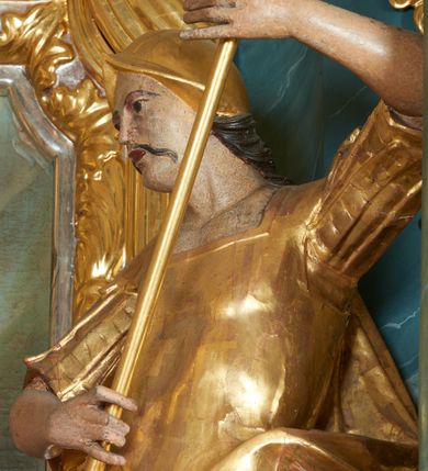 Zdjęcie nr 11: Ołtarz drewniany, prostopadłościenny z drewnianą mensą, w polu antepedium malowana na drewnie scena Zwiastowania (kopia obrazu Leonarda da Vinci). Na ołtarzu stoi tabliczka z kanonem w otoczeniu akantowych wolut tworzących podstawę dla pięciu lichtarzy utworzonych z ornamentu roślinnego. 
Nastawa architektoniczna, jednoosiowa, jednokondygnacyjna ze zwieńczeniem, ustawiona na dwustrefowym cokole, ujęta parą półfilarów i stojącą przed nimi parą kolumn dźwigających pełne belkowanie, przerwane nad polem środkowym. Na cokołach kolumn kanony w ornamentalnych ramach. Kolumny flankują od zewnątrz figury św. Tomasza (?) i św. Jana Nepomucena, od wewnątrz św. Michała Archanioła i św. Jerzego. W polu głównym obraz Matki Boskiej Szkaplerznej w formie stojącego prostokąta zamkniętego łukiem półkolistym nadwieszonym z uskokiem w profilowanej, dekorowanej ornamentem roślinnym ramie. Ponad nim kartusz ujęty ornamentem rocaille'owym i kratką regencyjną oraz uskrzydloną główką anielską flankowaną rocaille'ami. Zwieńczenie w formie leżącego prostokąta ujętego spływami wolutowymi dekorowanymi rocaille'ami, zamkniętego fragmentem falującego gzymsu z monogramem Marii w otoku z obłoków w glorii promienistej. W polu rzeźbiarskie przedstawienie św. Katarzyny Aleksandryjskiej flankowanej obłokami i wiązkami promieni oraz parą puttów. Na belkowaniu figury św. Rozalii i św. Calamindy. Ołtarz ujęty uszami utworzonymi z ornamentu rocaille'owego i kratki regencyjnej. Struktura polichromowana w sposób naśladujący marmoryzację w kolorze niebiesko-białym, profile i ornamentyka pozłacane.