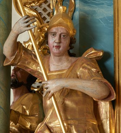 Zdjęcie nr 15: Ołtarz drewniany, prostopadłościenny z drewnianą mensą, w polu antepedium malowana na drewnie scena Zwiastowania (kopia obrazu Leonarda da Vinci). Na ołtarzu stoi tabliczka z kanonem w otoczeniu akantowych wolut tworzących podstawę dla pięciu lichtarzy utworzonych z ornamentu roślinnego. 
Nastawa architektoniczna, jednoosiowa, jednokondygnacyjna ze zwieńczeniem, ustawiona na dwustrefowym cokole, ujęta parą półfilarów i stojącą przed nimi parą kolumn dźwigających pełne belkowanie, przerwane nad polem środkowym. Na cokołach kolumn kanony w ornamentalnych ramach. Kolumny flankują od zewnątrz figury św. Tomasza (?) i św. Jana Nepomucena, od wewnątrz św. Michała Archanioła i św. Jerzego. W polu głównym obraz Matki Boskiej Szkaplerznej w formie stojącego prostokąta zamkniętego łukiem półkolistym nadwieszonym z uskokiem w profilowanej, dekorowanej ornamentem roślinnym ramie. Ponad nim kartusz ujęty ornamentem rocaille'owym i kratką regencyjną oraz uskrzydloną główką anielską flankowaną rocaille'ami. Zwieńczenie w formie leżącego prostokąta ujętego spływami wolutowymi dekorowanymi rocaille'ami, zamkniętego fragmentem falującego gzymsu z monogramem Marii w otoku z obłoków w glorii promienistej. W polu rzeźbiarskie przedstawienie św. Katarzyny Aleksandryjskiej flankowanej obłokami i wiązkami promieni oraz parą puttów. Na belkowaniu figury św. Rozalii i św. Calamindy. Ołtarz ujęty uszami utworzonymi z ornamentu rocaille'owego i kratki regencyjnej. Struktura polichromowana w sposób naśladujący marmoryzację w kolorze niebiesko-białym, profile i ornamentyka pozłacane.