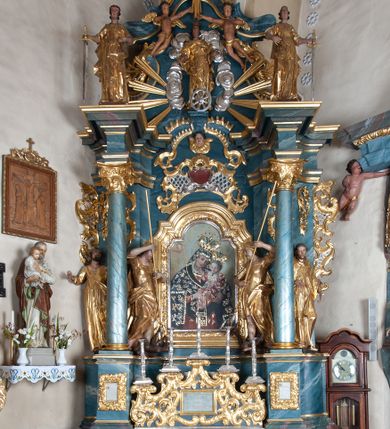 Zdjęcie nr 1: Ołtarz drewniany, prostopadłościenny z drewnianą mensą, w polu antepedium malowana na drewnie scena Zwiastowania (kopia obrazu Leonarda da Vinci). Na ołtarzu stoi tabliczka z kanonem w otoczeniu akantowych wolut tworzących podstawę dla pięciu lichtarzy utworzonych z ornamentu roślinnego. 
Nastawa architektoniczna, jednoosiowa, jednokondygnacyjna ze zwieńczeniem, ustawiona na dwustrefowym cokole, ujęta parą półfilarów i stojącą przed nimi parą kolumn dźwigających pełne belkowanie, przerwane nad polem środkowym. Na cokołach kolumn kanony w ornamentalnych ramach. Kolumny flankują od zewnątrz figury św. Tomasza (?) i św. Jana Nepomucena, od wewnątrz św. Michała Archanioła i św. Jerzego. W polu głównym obraz Matki Boskiej Szkaplerznej w formie stojącego prostokąta zamkniętego łukiem półkolistym nadwieszonym z uskokiem w profilowanej, dekorowanej ornamentem roślinnym ramie. Ponad nim kartusz ujęty ornamentem rocaille'owym i kratką regencyjną oraz uskrzydloną główką anielską flankowaną rocaille'ami. Zwieńczenie w formie leżącego prostokąta ujętego spływami wolutowymi dekorowanymi rocaille'ami, zamkniętego fragmentem falującego gzymsu z monogramem Marii w otoku z obłoków w glorii promienistej. W polu rzeźbiarskie przedstawienie św. Katarzyny Aleksandryjskiej flankowanej obłokami i wiązkami promieni oraz parą puttów. Na belkowaniu figury św. Rozalii i św. Calamindy. Ołtarz ujęty uszami utworzonymi z ornamentu rocaille'owego i kratki regencyjnej. Struktura polichromowana w sposób naśladujący marmoryzację w kolorze niebiesko-białym, profile i ornamentyka pozłacane.