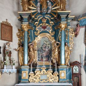Zdjęcie nr 1: Ołtarz drewniany, prostopadłościenny z drewnianą mensą, w polu antepedium malowana na drewnie scena Zwiastowania (kopia obrazu Leonarda da Vinci). Na ołtarzu stoi tabliczka z kanonem w otoczeniu akantowych wolut tworzących podstawę dla pięciu lichtarzy utworzonych z ornamentu roślinnego. 
Nastawa architektoniczna, jednoosiowa, jednokondygnacyjna ze zwieńczeniem, ustawiona na dwustrefowym cokole, ujęta parą półfilarów i stojącą przed nimi parą kolumn dźwigających pełne belkowanie, przerwane nad polem środkowym. Na cokołach kolumn kanony w ornamentalnych ramach. Kolumny flankują od zewnątrz figury św. Tomasza (?) i św. Jana Nepomucena, od wewnątrz św. Michała Archanioła i św. Jerzego. W polu głównym obraz Matki Boskiej Szkaplerznej w formie stojącego prostokąta zamkniętego łukiem półkolistym nadwieszonym z uskokiem w profilowanej, dekorowanej ornamentem roślinnym ramie. Ponad nim kartusz ujęty ornamentem rocaille'owym i kratką regencyjną oraz uskrzydloną główką anielską flankowaną rocaille'ami. Zwieńczenie w formie leżącego prostokąta ujętego spływami wolutowymi dekorowanymi rocaille'ami, zamkniętego fragmentem falującego gzymsu z monogramem Marii w otoku z obłoków w glorii promienistej. W polu rzeźbiarskie przedstawienie św. Katarzyny Aleksandryjskiej flankowanej obłokami i wiązkami promieni oraz parą puttów. Na belkowaniu figury św. Rozalii i św. Calamindy. Ołtarz ujęty uszami utworzonymi z ornamentu rocaille'owego i kratki regencyjnej. Struktura polichromowana w sposób naśladujący marmoryzację w kolorze niebiesko-białym, profile i ornamentyka pozłacane.