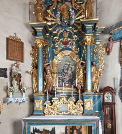 Zdjęcie nr 2: Ołtarz drewniany, prostopadłościenny z drewnianą mensą, w polu antepedium malowana na drewnie scena Zwiastowania (kopia obrazu Leonarda da Vinci). Na ołtarzu stoi tabliczka z kanonem w otoczeniu akantowych wolut tworzących podstawę dla pięciu lichtarzy utworzonych z ornamentu roślinnego. 
Nastawa architektoniczna, jednoosiowa, jednokondygnacyjna ze zwieńczeniem, ustawiona na dwustrefowym cokole, ujęta parą półfilarów i stojącą przed nimi parą kolumn dźwigających pełne belkowanie, przerwane nad polem środkowym. Na cokołach kolumn kanony w ornamentalnych ramach. Kolumny flankują od zewnątrz figury św. Tomasza (?) i św. Jana Nepomucena, od wewnątrz św. Michała Archanioła i św. Jerzego. W polu głównym obraz Matki Boskiej Szkaplerznej w formie stojącego prostokąta zamkniętego łukiem półkolistym nadwieszonym z uskokiem w profilowanej, dekorowanej ornamentem roślinnym ramie. Ponad nim kartusz ujęty ornamentem rocaille'owym i kratką regencyjną oraz uskrzydloną główką anielską flankowaną rocaille'ami. Zwieńczenie w formie leżącego prostokąta ujętego spływami wolutowymi dekorowanymi rocaille'ami, zamkniętego fragmentem falującego gzymsu z monogramem Marii w otoku z obłoków w glorii promienistej. W polu rzeźbiarskie przedstawienie św. Katarzyny Aleksandryjskiej flankowanej obłokami i wiązkami promieni oraz parą puttów. Na belkowaniu figury św. Rozalii i św. Calamindy. Ołtarz ujęty uszami utworzonymi z ornamentu rocaille'owego i kratki regencyjnej. Struktura polichromowana w sposób naśladujący marmoryzację w kolorze niebiesko-białym, profile i ornamentyka pozłacane.