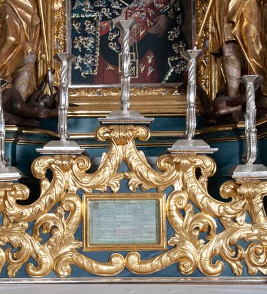 Zdjęcie nr 19: Ołtarz drewniany, prostopadłościenny z drewnianą mensą, w polu antepedium malowana na drewnie scena Zwiastowania (kopia obrazu Leonarda da Vinci). Na ołtarzu stoi tabliczka z kanonem w otoczeniu akantowych wolut tworzących podstawę dla pięciu lichtarzy utworzonych z ornamentu roślinnego. 
Nastawa architektoniczna, jednoosiowa, jednokondygnacyjna ze zwieńczeniem, ustawiona na dwustrefowym cokole, ujęta parą półfilarów i stojącą przed nimi parą kolumn dźwigających pełne belkowanie, przerwane nad polem środkowym. Na cokołach kolumn kanony w ornamentalnych ramach. Kolumny flankują od zewnątrz figury św. Tomasza (?) i św. Jana Nepomucena, od wewnątrz św. Michała Archanioła i św. Jerzego. W polu głównym obraz Matki Boskiej Szkaplerznej w formie stojącego prostokąta zamkniętego łukiem półkolistym nadwieszonym z uskokiem w profilowanej, dekorowanej ornamentem roślinnym ramie. Ponad nim kartusz ujęty ornamentem rocaille'owym i kratką regencyjną oraz uskrzydloną główką anielską flankowaną rocaille'ami. Zwieńczenie w formie leżącego prostokąta ujętego spływami wolutowymi dekorowanymi rocaille'ami, zamkniętego fragmentem falującego gzymsu z monogramem Marii w otoku z obłoków w glorii promienistej. W polu rzeźbiarskie przedstawienie św. Katarzyny Aleksandryjskiej flankowanej obłokami i wiązkami promieni oraz parą puttów. Na belkowaniu figury św. Rozalii i św. Calamindy. Ołtarz ujęty uszami utworzonymi z ornamentu rocaille'owego i kratki regencyjnej. Struktura polichromowana w sposób naśladujący marmoryzację w kolorze niebiesko-białym, profile i ornamentyka pozłacane.