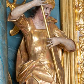 Zdjęcie nr 1: Figura ścięta z tyłu, drążona, zwrócona w trzech czwartych w prawo, w kontrapoście. Święty obiema rękami trzyma włócznię skierowaną w dół w stronę leżącego u jego stóp diabła. Twarz ma pociągłą, o migdałowatych oczach, lekko garbatym nosie, pełnych ustach, okoloną długimi, silnie kręconymi włosami. Postać w stroju żołnierza, w tunice sięgającej kolan, zbroi oraz w płaszczu zarzuconym na plecy i opadającym na prawą nogę, przewiązanym taśmą przez tors, na głowie ma hełm. Ciało polichromowane naturalistycznie, strój złocony. 
