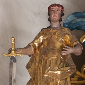 Zdjęcie nr 1: Figura ścięta z tyłu. Święta przedstawiona jest w całej postaci, stojąca frontalnie, z lekko ugiętą lewą nogą. W prawej dłoni trzyma miecz zwrócony ostrzem w dół, lewą rękę wyciąga przed siebie. Twarz ma podłużną o pełnych policzkach i drugim podbródku, migdałowatych oczach, prostym nosie, okoloną silnie kręconymi włosami opadającymi na plecy. Święta ubrana jest w suknię z dekoltem, z podwiniętymi rękawami, spiętą w talii gorsetem oraz płaszcz opadający na plecy i lewy bok postaci. Na głowie ma wieniec z róż. Polichromia naturalistyczna w partiach ciała, szaty złocone, ostrze miecza srebrzone. 

