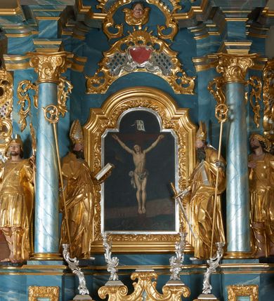 Zdjęcie nr 2: Ołtarz drewniany, prostopadłościenny z drewnianą mensą, w polu antepedium malowana na drewnie scena Ukrzyżowania. Na ołtarzu stoi tabliczka z kanonem w otoczeniu akantowych wolut tworzących podstawę dla pięciu lichtarzy utworzonych z ornamentu roślinnego (brak środkowego). 
Nastawa architektoniczna, jednoosiowa, jednokondygnacyjna ze zwieńczeniem, ustawiona na dwustrefowym cokole, ujęta parą półfilarów i stojącą przed nimi parą kolumn dźwigających pełne belkowanie, przerwane nad polem środkowym. Na cokołach kolumn kanony w ornamentalnych ramach. Kolumny flankują od zewnątrz figury św. Floriana i św. Longina, od wewnątrz św. Donata i św. Marcina. W polu głównym obraz Ukrzyżowania w formie stojącego prostokąta zamkniętego łukiem półkolistym nadwieszonym z uskokiem w profilowanej, dekorowanej ornamentem roślinnym ramie. Ponad nim kartusz ujęty ornamentem rocaille'owym i kratką regencyjną oraz uskrzydlona główka anielska flankowana rocaille'ami. Zwieńczenie w formie leżącego prostokąta ujętego spływami wolutowymi dekorowanymi rocaille'ami, zamkniętego fragmentem falującego gzymsu z monogramem IHS w otoku z obłoków w glorii promienistej. W polu rzeźbiarskie przedstawienie św. Antoniego Padewskiego flankowanego obłokami i wiązkami promieni oraz parą puttów. Na belkowaniu figury św. Walentego i św. Jana Chryzostoma. Ołtarz ujęty uszami utworzonymi z ornamentu rocaille'owego i kratki regencyjnej. Struktura polichromowana w sposób naśladujący marmoryzację w kolorze niebiesko-białym, profile i ornamentyka pozłacane.
