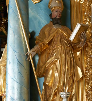Zdjęcie nr 10: Ołtarz drewniany, prostopadłościenny z drewnianą mensą, w polu antepedium malowana na drewnie scena Ukrzyżowania. Na ołtarzu stoi tabliczka z kanonem w otoczeniu akantowych wolut tworzących podstawę dla pięciu lichtarzy utworzonych z ornamentu roślinnego (brak środkowego). 
Nastawa architektoniczna, jednoosiowa, jednokondygnacyjna ze zwieńczeniem, ustawiona na dwustrefowym cokole, ujęta parą półfilarów i stojącą przed nimi parą kolumn dźwigających pełne belkowanie, przerwane nad polem środkowym. Na cokołach kolumn kanony w ornamentalnych ramach. Kolumny flankują od zewnątrz figury św. Floriana i św. Longina, od wewnątrz św. Donata i św. Marcina. W polu głównym obraz Ukrzyżowania w formie stojącego prostokąta zamkniętego łukiem półkolistym nadwieszonym z uskokiem w profilowanej, dekorowanej ornamentem roślinnym ramie. Ponad nim kartusz ujęty ornamentem rocaille'owym i kratką regencyjną oraz uskrzydlona główka anielska flankowana rocaille'ami. Zwieńczenie w formie leżącego prostokąta ujętego spływami wolutowymi dekorowanymi rocaille'ami, zamkniętego fragmentem falującego gzymsu z monogramem IHS w otoku z obłoków w glorii promienistej. W polu rzeźbiarskie przedstawienie św. Antoniego Padewskiego flankowanego obłokami i wiązkami promieni oraz parą puttów. Na belkowaniu figury św. Walentego i św. Jana Chryzostoma. Ołtarz ujęty uszami utworzonymi z ornamentu rocaille'owego i kratki regencyjnej. Struktura polichromowana w sposób naśladujący marmoryzację w kolorze niebiesko-białym, profile i ornamentyka pozłacane.
