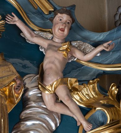 Zdjęcie nr 4: Figura ścięta z tyłu. Święty przedstawiony jest w całej postaci, frontalnie, w kontrapoście, delikatnie przechylony w tył. Lewą rękę zgiętą w łokciu wyciąga w przód, w prawej, zgiętej trzyma księgę, na której siedzi Dzieciątko. Twarz ma pociągłą, o pełnych policzkach, migdałowatych oczach, prostym nosie i pełnych ustach, z silnie zaznaczoną brodą i podbródkiem, okoloną krótkimi, kręconymi włosami. Święty ubrany jest w habit przewiązany w pasie podwójnym sznurem i pelerynkę. Nad jego głową nimb w formie glorii promienistej. Dzieciątko zwrócone jest profilem w prawo, lewą ręką ujmuje twarz świętego, prawą wyciąga w bok. Twarz ma pociągłą o pełnych policzkach, okoloną kręconymi włosami, ciało zaś ma szczupłe, w partii bioder przykryte tkaniną. Polichromia naturalistyczna w partiach ciała, szaty i gloria pozłocone.
