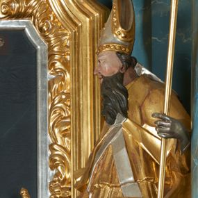 Zdjęcie nr 1: Rzeźba ścięta z tyłu, drążona, zwrócona frontalnie, z głową skierowaną w prawą stronę, w kontrapoście, z lekko odchyloną w tył sylwetką. Święty w prawej ręce trzyma miecz skierowany ostrzem w dół, w lewej pastorał. Twarz ma pociągłą, o zapadniętych policzkach, dużych, migdałowatych oczach, lekko garbatym nosie, pełnych rozchylonych ustach, okoloną wąsami i długą, falistą brodą, opadającą na pierś oraz krótkimi, kręconymi włosami. Ubrany jest w strój biskupa: albę przewiązaną w pasie, skrzyżowaną stułę, kapę zapiętą na piersi z fragmentem materiału zawiniętym na lewej nodze, na głowie ma infułę, na dłoniach rękawiczki. Ciało polichromowane naturalistycznie, strój i atrybuty pozłocone i posrebrzone. 