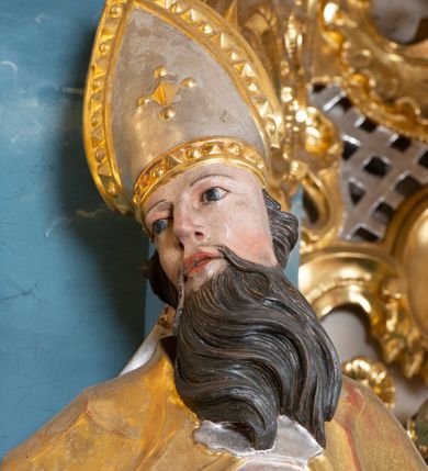 Zdjęcie nr 3: Rzeźba ścięta z tyłu, drążona, zwrócona frontalnie, z głową skierowaną w prawą stronę, w kontrapoście, z lekko odchyloną w tył sylwetką. Święty w prawej ręce trzyma miecz skierowany ostrzem w dół, w lewej pastorał. Twarz ma pociągłą, o zapadniętych policzkach, dużych, migdałowatych oczach, lekko garbatym nosie, pełnych rozchylonych ustach, okoloną wąsami i długą, falistą brodą, opadającą na pierś oraz krótkimi, kręconymi włosami. Ubrany jest w strój biskupa: albę przewiązaną w pasie, skrzyżowaną stułę, kapę zapiętą na piersi z fragmentem materiału zawiniętym na lewej nodze, na głowie ma infułę, na dłoniach rękawiczki. Ciało polichromowane naturalistycznie, strój i atrybuty pozłocone i posrebrzone. 