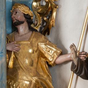 Zdjęcie nr 1: Rzeźba ścięta z tyłu, drążona, zwrócona frontalnie, z głową skierowaną w prawo, w kontrapoście. Święty w lewej ręce trzyma włócznię, prawa spoczywa na piersi. Twarz ma okrągłą o migdałowatych oczach, lekko garbatym nosie i pełnych ustach, okoloną krótką brodą i wąsami oraz długimi silnie skręconymi włosami opadającymi na plecy. Postać ubrana jest w tunikę sięgającą kolan, rzymską zbroję z piórami oraz płaszcz zawieszony na taśmie, opadający na lewy bok. Na głowie ma wieniec laurowy, na nogach wysokie sandały. Ciało polichromowane naturalistycznie, szaty i atrybuty złocone. 