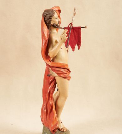 Zdjęcie nr 3: Rzeźba pełnoplastyczna, ustawiona na podstawie o nieregularnym planie, imitującej fragment podłoża. Chrystus ukazany frontalnie, w wykroku, w lewej wyciągniętej w bok ręce trzyma drzewce czerwonej, materiałowej chorągwi, zakończone krzyżem, prawą ugiętą, unosi w geście błogosławieństwa. Twarz ma szczupłą i pociągłą, o wąskich, migdałowatych oczach, szerokim nosie i niewielkich ustach; okoloną krótką brodą oraz silnie skręconymi w pukle włosami, opadającymi na ramiona. Chrystus w partii bioder przewiązany krótkim, przylegającym, srebrzonym perizonium. Przez prawe udo i lewe ramię ma przewiązany czerwony, silnie drapowany płaszcz, rozwiany półkoliście z tyłu postaci oraz opadający po bokach. Ciało Chrystusa szczupłe, niemal pozbawione modelunku. Polichromia ciała figury naturalistyczna, o jasnej karnacji. 



