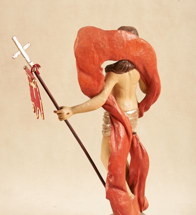 Zdjęcie nr 5: Rzeźba pełnoplastyczna, ustawiona na podstawie o nieregularnym planie, imitującej fragment podłoża. Chrystus ukazany frontalnie, w wykroku, w lewej wyciągniętej w bok ręce trzyma drzewce czerwonej, materiałowej chorągwi, zakończone krzyżem, prawą ugiętą, unosi w geście błogosławieństwa. Twarz ma szczupłą i pociągłą, o wąskich, migdałowatych oczach, szerokim nosie i niewielkich ustach; okoloną krótką brodą oraz silnie skręconymi w pukle włosami, opadającymi na ramiona. Chrystus w partii bioder przewiązany krótkim, przylegającym, srebrzonym perizonium. Przez prawe udo i lewe ramię ma przewiązany czerwony, silnie drapowany płaszcz, rozwiany półkoliście z tyłu postaci oraz opadający po bokach. Ciało Chrystusa szczupłe, niemal pozbawione modelunku. Polichromia ciała figury naturalistyczna, o jasnej karnacji. 



