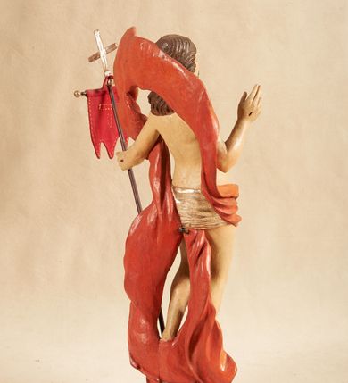 Zdjęcie nr 4: Rzeźba pełnoplastyczna, ustawiona na podstawie o nieregularnym planie, imitującej fragment podłoża. Chrystus ukazany frontalnie, w wykroku, w lewej wyciągniętej w bok ręce trzyma drzewce czerwonej, materiałowej chorągwi, zakończone krzyżem, prawą ugiętą, unosi w geście błogosławieństwa. Twarz ma szczupłą i pociągłą, o wąskich, migdałowatych oczach, szerokim nosie i niewielkich ustach; okoloną krótką brodą oraz silnie skręconymi w pukle włosami, opadającymi na ramiona. Chrystus w partii bioder przewiązany krótkim, przylegającym, srebrzonym perizonium. Przez prawe udo i lewe ramię ma przewiązany czerwony, silnie drapowany płaszcz, rozwiany półkoliście z tyłu postaci oraz opadający po bokach. Ciało Chrystusa szczupłe, niemal pozbawione modelunku. Polichromia ciała figury naturalistyczna, o jasnej karnacji. 



