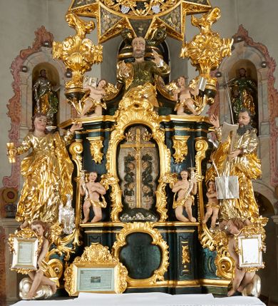 Zdjęcie nr 1: Ołtarz dwustronny, sarkofagowy, dekorowany rocaille'm, mensa drewniana na planie kwadratu, od frontu z kamiennym portatylem.
Nastawa ołtarzowa dwustronna, na rzucie leżącej litery X, w formie  rozbudowanego tabernakulum z tronem wystawienia. Obie strony są analogiczne pod względem architektonicznym. Tabernakulum na cokole, o wypukłej ściance frontowej, flankowanej parą pilastrów o trzonach dekorowanym płycinami z rocaille'm, dźwigających gzyms wieńczący. W polu drzwiczki ujęte rokokowym kartuszem. Na tabernakulum tron wystawienia o wklęsło-wypukłym licu, ujęty parą impostów podtrzymywanych przez rocaille'owe konsole oraz pilastrami w narożach, których trzony przyjmują formę spływów wolutowych, sięgające podstawy tabernakulum, na których stoją figury. W polu środkowym tronu wystawienia znajduje się obrotowa nisza o nieregularnym kształcie ujęta obramieniem z rocaille'u, przesłonięta wypukłą ścianką z płaskorzeźbionym krucyfiksem  i winnym gronem, zwieńczona rzeźbioną półpostacią. Całość wieńczy cokół z dwoma ramionami, na których stoją rocaille'owe wazony. Na cokole osadzona jest dużych rozmiarów, dwustronna, dwunastoramienna gwiazda relikwiarzowa, miażdżąca węża. Gwiazda z obu stron ujęta jest kilkoma pierścieniami z winnego grona oraz ornamentu roślinnego, w ramionach oraz w polu głównym umieszczone są za szkłem relikwie wśród kwiatowych dekoracji. 
Na awersie ołtarza, na mensie znajdują się dwie figurki puttów siedzących na obłokach i trzymających tabliczki z kanonami. Całość flankują ustawione na spływach wolutowych figury św. Jana Ewangelisty i św. Bartłomieja, tron wieńczy półpostać Boga Ojca, ujęta przez dwa putta z otwartymi księgami. Obrotową niszę flankują dwa aniołki trzymające lichtarze. Na rewersie ołtarza na spływach wolutowych stoją figury św. Andrzeja i św. Piotra, tron wieńczy półpostać Mojżesza flankowana przez dwa putta z otwartymi księgami.
Struktura polichromowana w kolorze ciemnozielonym, ornamentyka i profile złocone, detal srebrzony.
