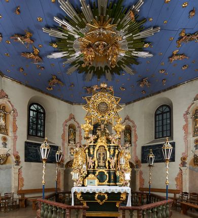 Zdjęcie nr 6: Ołtarz dwustronny, sarkofagowy, dekorowany rocaille'm, mensa drewniana na planie kwadratu, od frontu z kamiennym portatylem.
Nastawa ołtarzowa dwustronna, na rzucie leżącej litery X, w formie  rozbudowanego tabernakulum z tronem wystawienia. Obie strony są analogiczne pod względem architektonicznym. Tabernakulum na cokole, o wypukłej ściance frontowej, flankowanej parą pilastrów o trzonach dekorowanym płycinami z rocaille'm, dźwigających gzyms wieńczący. W polu drzwiczki ujęte rokokowym kartuszem. Na tabernakulum tron wystawienia o wklęsło-wypukłym licu, ujęty parą impostów podtrzymywanych przez rocaille'owe konsole oraz pilastrami w narożach, których trzony przyjmują formę spływów wolutowych, sięgające podstawy tabernakulum, na których stoją figury. W polu środkowym tronu wystawienia znajduje się obrotowa nisza o nieregularnym kształcie ujęta obramieniem z rocaille'u, przesłonięta wypukłą ścianką z płaskorzeźbionym krucyfiksem  i winnym gronem, zwieńczona rzeźbioną półpostacią. Całość wieńczy cokół z dwoma ramionami, na których stoją rocaille'owe wazony. Na cokole osadzona jest dużych rozmiarów, dwustronna, dwunastoramienna gwiazda relikwiarzowa, miażdżąca węża. Gwiazda z obu stron ujęta jest kilkoma pierścieniami z winnego grona oraz ornamentu roślinnego, w ramionach oraz w polu głównym umieszczone są za szkłem relikwie wśród kwiatowych dekoracji. 
Na awersie ołtarza, na mensie znajdują się dwie figurki puttów siedzących na obłokach i trzymających tabliczki z kanonami. Całość flankują ustawione na spływach wolutowych figury św. Jana Ewangelisty i św. Bartłomieja, tron wieńczy półpostać Boga Ojca, ujęta przez dwa putta z otwartymi księgami. Obrotową niszę flankują dwa aniołki trzymające lichtarze. Na rewersie ołtarza na spływach wolutowych stoją figury św. Andrzeja i św. Piotra, tron wieńczy półpostać Mojżesza flankowana przez dwa putta z otwartymi księgami.
Struktura polichromowana w kolorze ciemnozielonym, ornamentyka i profile złocone, detal srebrzony.
