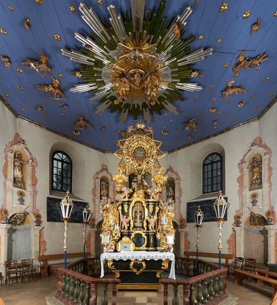 Zdjęcie nr 5: Ołtarz dwustronny, sarkofagowy, dekorowany rocaille'm, mensa drewniana na planie kwadratu, od frontu z kamiennym portatylem.
Nastawa ołtarzowa dwustronna, na rzucie leżącej litery X, w formie  rozbudowanego tabernakulum z tronem wystawienia. Obie strony są analogiczne pod względem architektonicznym. Tabernakulum na cokole, o wypukłej ściance frontowej, flankowanej parą pilastrów o trzonach dekorowanym płycinami z rocaille'm, dźwigających gzyms wieńczący. W polu drzwiczki ujęte rokokowym kartuszem. Na tabernakulum tron wystawienia o wklęsło-wypukłym licu, ujęty parą impostów podtrzymywanych przez rocaille'owe konsole oraz pilastrami w narożach, których trzony przyjmują formę spływów wolutowych, sięgające podstawy tabernakulum, na których stoją figury. W polu środkowym tronu wystawienia znajduje się obrotowa nisza o nieregularnym kształcie ujęta obramieniem z rocaille'u, przesłonięta wypukłą ścianką z płaskorzeźbionym krucyfiksem  i winnym gronem, zwieńczona rzeźbioną półpostacią. Całość wieńczy cokół z dwoma ramionami, na których stoją rocaille'owe wazony. Na cokole osadzona jest dużych rozmiarów, dwustronna, dwunastoramienna gwiazda relikwiarzowa, miażdżąca węża. Gwiazda z obu stron ujęta jest kilkoma pierścieniami z winnego grona oraz ornamentu roślinnego, w ramionach oraz w polu głównym umieszczone są za szkłem relikwie wśród kwiatowych dekoracji. 
Na awersie ołtarza, na mensie znajdują się dwie figurki puttów siedzących na obłokach i trzymających tabliczki z kanonami. Całość flankują ustawione na spływach wolutowych figury św. Jana Ewangelisty i św. Bartłomieja, tron wieńczy półpostać Boga Ojca, ujęta przez dwa putta z otwartymi księgami. Obrotową niszę flankują dwa aniołki trzymające lichtarze. Na rewersie ołtarza na spływach wolutowych stoją figury św. Andrzeja i św. Piotra, tron wieńczy półpostać Mojżesza flankowana przez dwa putta z otwartymi księgami.
Struktura polichromowana w kolorze ciemnozielonym, ornamentyka i profile złocone, detal srebrzony.
