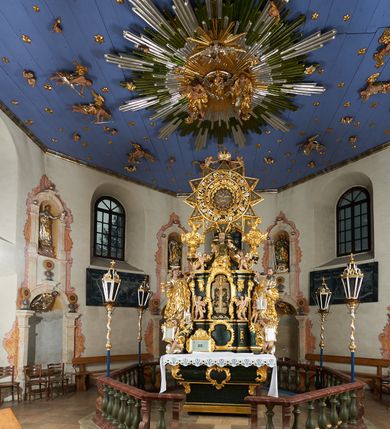 Zdjęcie nr 4: Ołtarz dwustronny, sarkofagowy, dekorowany rocaille'm, mensa drewniana na planie kwadratu, od frontu z kamiennym portatylem.
Nastawa ołtarzowa dwustronna, na rzucie leżącej litery X, w formie  rozbudowanego tabernakulum z tronem wystawienia. Obie strony są analogiczne pod względem architektonicznym. Tabernakulum na cokole, o wypukłej ściance frontowej, flankowanej parą pilastrów o trzonach dekorowanym płycinami z rocaille'm, dźwigających gzyms wieńczący. W polu drzwiczki ujęte rokokowym kartuszem. Na tabernakulum tron wystawienia o wklęsło-wypukłym licu, ujęty parą impostów podtrzymywanych przez rocaille'owe konsole oraz pilastrami w narożach, których trzony przyjmują formę spływów wolutowych, sięgające podstawy tabernakulum, na których stoją figury. W polu środkowym tronu wystawienia znajduje się obrotowa nisza o nieregularnym kształcie ujęta obramieniem z rocaille'u, przesłonięta wypukłą ścianką z płaskorzeźbionym krucyfiksem  i winnym gronem, zwieńczona rzeźbioną półpostacią. Całość wieńczy cokół z dwoma ramionami, na których stoją rocaille'owe wazony. Na cokole osadzona jest dużych rozmiarów, dwustronna, dwunastoramienna gwiazda relikwiarzowa, miażdżąca węża. Gwiazda z obu stron ujęta jest kilkoma pierścieniami z winnego grona oraz ornamentu roślinnego, w ramionach oraz w polu głównym umieszczone są za szkłem relikwie wśród kwiatowych dekoracji. 
Na awersie ołtarza, na mensie znajdują się dwie figurki puttów siedzących na obłokach i trzymających tabliczki z kanonami. Całość flankują ustawione na spływach wolutowych figury św. Jana Ewangelisty i św. Bartłomieja, tron wieńczy półpostać Boga Ojca, ujęta przez dwa putta z otwartymi księgami. Obrotową niszę flankują dwa aniołki trzymające lichtarze. Na rewersie ołtarza na spływach wolutowych stoją figury św. Andrzeja i św. Piotra, tron wieńczy półpostać Mojżesza flankowana przez dwa putta z otwartymi księgami.
Struktura polichromowana w kolorze ciemnozielonym, ornamentyka i profile złocone, detal srebrzony.
