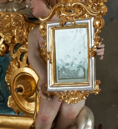 Zdjęcie nr 42: Ołtarz dwustronny, sarkofagowy, dekorowany rocaille'm, mensa drewniana na planie kwadratu, od frontu z kamiennym portatylem.
Nastawa ołtarzowa dwustronna, na rzucie leżącej litery X, w formie  rozbudowanego tabernakulum z tronem wystawienia. Obie strony są analogiczne pod względem architektonicznym. Tabernakulum na cokole, o wypukłej ściance frontowej, flankowanej parą pilastrów o trzonach dekorowanym płycinami z rocaille'm, dźwigających gzyms wieńczący. W polu drzwiczki ujęte rokokowym kartuszem. Na tabernakulum tron wystawienia o wklęsło-wypukłym licu, ujęty parą impostów podtrzymywanych przez rocaille'owe konsole oraz pilastrami w narożach, których trzony przyjmują formę spływów wolutowych, sięgające podstawy tabernakulum, na których stoją figury. W polu środkowym tronu wystawienia znajduje się obrotowa nisza o nieregularnym kształcie ujęta obramieniem z rocaille'u, przesłonięta wypukłą ścianką z płaskorzeźbionym krucyfiksem  i winnym gronem, zwieńczona rzeźbioną półpostacią. Całość wieńczy cokół z dwoma ramionami, na których stoją rocaille'owe wazony. Na cokole osadzona jest dużych rozmiarów, dwustronna, dwunastoramienna gwiazda relikwiarzowa, miażdżąca węża. Gwiazda z obu stron ujęta jest kilkoma pierścieniami z winnego grona oraz ornamentu roślinnego, w ramionach oraz w polu głównym umieszczone są za szkłem relikwie wśród kwiatowych dekoracji. 
Na awersie ołtarza, na mensie znajdują się dwie figurki puttów siedzących na obłokach i trzymających tabliczki z kanonami. Całość flankują ustawione na spływach wolutowych figury św. Jana Ewangelisty i św. Bartłomieja, tron wieńczy półpostać Boga Ojca, ujęta przez dwa putta z otwartymi księgami. Obrotową niszę flankują dwa aniołki trzymające lichtarze. Na rewersie ołtarza na spływach wolutowych stoją figury św. Andrzeja i św. Piotra, tron wieńczy półpostać Mojżesza flankowana przez dwa putta z otwartymi księgami.
Struktura polichromowana w kolorze ciemnozielonym, ornamentyka i profile złocone, detal srebrzony.
