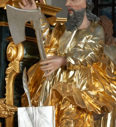 Zdjęcie nr 39: Ołtarz dwustronny, sarkofagowy, dekorowany rocaille&#039;m, mensa drewniana na planie kwadratu, od frontu z kamiennym portatylem.
Nastawa ołtarzowa dwustronna, na rzucie leżącej litery X, w formie  rozbudowanego tabernakulum z tronem wystawienia. Obie strony są analogiczne pod względem architektonicznym. Tabernakulum na cokole, o wypukłej ściance frontowej, flankowanej parą pilastrów o trzonach dekorowanym płycinami z rocaille&#039;m, dźwigających gzyms wieńczący. W polu drzwiczki ujęte rokokowym kartuszem. Na tabernakulum tron wystawienia o wklęsło-wypukłym licu, ujęty parą impostów podtrzymywanych przez rocaille&#039;owe konsole oraz pilastrami w narożach, których trzony przyjmują formę spływów wolutowych, sięgające podstawy tabernakulum, na których stoją figury. W polu środkowym tronu wystawienia znajduje się obrotowa nisza o nieregularnym kształcie ujęta obramieniem z rocaille&#039;u, przesłonięta wypukłą ścianką z płaskorzeźbionym krucyfiksem  i winnym gronem, zwieńczona rzeźbioną półpostacią. Całość wieńczy cokół z dwoma ramionami, na których stoją rocaille&#039;owe wazony. Na cokole osadzona jest dużych rozmiarów, dwustronna, dwunastoramienna gwiazda relikwiarzowa, miażdżąca węża. Gwiazda z obu stron ujęta jest kilkoma pierścieniami z winnego grona oraz ornamentu roślinnego, w ramionach oraz w polu głównym umieszczone są za szkłem relikwie wśród kwiatowych dekoracji. 
Na awersie ołtarza, na mensie znajdują się dwie figurki puttów siedzących na obłokach i trzymających tabliczki z kanonami. Całość flankują ustawione na spływach wolutowych figury św. Jana Ewangelisty i św. Bartłomieja, tron wieńczy półpostać Boga Ojca, ujęta przez dwa putta z otwartymi księgami. Obrotową niszę flankują dwa aniołki trzymające lichtarze. Na rewersie ołtarza na spływach wolutowych stoją figury św. Andrzeja i św. Piotra, tron wieńczy półpostać Mojżesza flankowana przez dwa putta z otwartymi księgami.
Struktura polichromowana w kolorze ciemnozielonym, ornamentyka i profile złocone, detal srebrzony.
