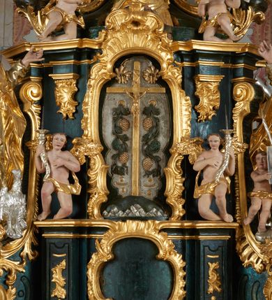 Zdjęcie nr 14: Ołtarz dwustronny, sarkofagowy, dekorowany rocaille'm, mensa drewniana na planie kwadratu, od frontu z kamiennym portatylem.
Nastawa ołtarzowa dwustronna, na rzucie leżącej litery X, w formie  rozbudowanego tabernakulum z tronem wystawienia. Obie strony są analogiczne pod względem architektonicznym. Tabernakulum na cokole, o wypukłej ściance frontowej, flankowanej parą pilastrów o trzonach dekorowanym płycinami z rocaille'm, dźwigających gzyms wieńczący. W polu drzwiczki ujęte rokokowym kartuszem. Na tabernakulum tron wystawienia o wklęsło-wypukłym licu, ujęty parą impostów podtrzymywanych przez rocaille'owe konsole oraz pilastrami w narożach, których trzony przyjmują formę spływów wolutowych, sięgające podstawy tabernakulum, na których stoją figury. W polu środkowym tronu wystawienia znajduje się obrotowa nisza o nieregularnym kształcie ujęta obramieniem z rocaille'u, przesłonięta wypukłą ścianką z płaskorzeźbionym krucyfiksem  i winnym gronem, zwieńczona rzeźbioną półpostacią. Całość wieńczy cokół z dwoma ramionami, na których stoją rocaille'owe wazony. Na cokole osadzona jest dużych rozmiarów, dwustronna, dwunastoramienna gwiazda relikwiarzowa, miażdżąca węża. Gwiazda z obu stron ujęta jest kilkoma pierścieniami z winnego grona oraz ornamentu roślinnego, w ramionach oraz w polu głównym umieszczone są za szkłem relikwie wśród kwiatowych dekoracji. 
Na awersie ołtarza, na mensie znajdują się dwie figurki puttów siedzących na obłokach i trzymających tabliczki z kanonami. Całość flankują ustawione na spływach wolutowych figury św. Jana Ewangelisty i św. Bartłomieja, tron wieńczy półpostać Boga Ojca, ujęta przez dwa putta z otwartymi księgami. Obrotową niszę flankują dwa aniołki trzymające lichtarze. Na rewersie ołtarza na spływach wolutowych stoją figury św. Andrzeja i św. Piotra, tron wieńczy półpostać Mojżesza flankowana przez dwa putta z otwartymi księgami.
Struktura polichromowana w kolorze ciemnozielonym, ornamentyka i profile złocone, detal srebrzony.
