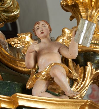 Zdjęcie nr 32: Ołtarz dwustronny, sarkofagowy, dekorowany rocaille'm, mensa drewniana na planie kwadratu, od frontu z kamiennym portatylem.
Nastawa ołtarzowa dwustronna, na rzucie leżącej litery X, w formie  rozbudowanego tabernakulum z tronem wystawienia. Obie strony są analogiczne pod względem architektonicznym. Tabernakulum na cokole, o wypukłej ściance frontowej, flankowanej parą pilastrów o trzonach dekorowanym płycinami z rocaille'm, dźwigających gzyms wieńczący. W polu drzwiczki ujęte rokokowym kartuszem. Na tabernakulum tron wystawienia o wklęsło-wypukłym licu, ujęty parą impostów podtrzymywanych przez rocaille'owe konsole oraz pilastrami w narożach, których trzony przyjmują formę spływów wolutowych, sięgające podstawy tabernakulum, na których stoją figury. W polu środkowym tronu wystawienia znajduje się obrotowa nisza o nieregularnym kształcie ujęta obramieniem z rocaille'u, przesłonięta wypukłą ścianką z płaskorzeźbionym krucyfiksem  i winnym gronem, zwieńczona rzeźbioną półpostacią. Całość wieńczy cokół z dwoma ramionami, na których stoją rocaille'owe wazony. Na cokole osadzona jest dużych rozmiarów, dwustronna, dwunastoramienna gwiazda relikwiarzowa, miażdżąca węża. Gwiazda z obu stron ujęta jest kilkoma pierścieniami z winnego grona oraz ornamentu roślinnego, w ramionach oraz w polu głównym umieszczone są za szkłem relikwie wśród kwiatowych dekoracji. 
Na awersie ołtarza, na mensie znajdują się dwie figurki puttów siedzących na obłokach i trzymających tabliczki z kanonami. Całość flankują ustawione na spływach wolutowych figury św. Jana Ewangelisty i św. Bartłomieja, tron wieńczy półpostać Boga Ojca, ujęta przez dwa putta z otwartymi księgami. Obrotową niszę flankują dwa aniołki trzymające lichtarze. Na rewersie ołtarza na spływach wolutowych stoją figury św. Andrzeja i św. Piotra, tron wieńczy półpostać Mojżesza flankowana przez dwa putta z otwartymi księgami.
Struktura polichromowana w kolorze ciemnozielonym, ornamentyka i profile złocone, detal srebrzony.
