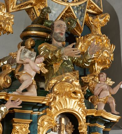 Zdjęcie nr 16: Ołtarz dwustronny, sarkofagowy, dekorowany rocaille'm, mensa drewniana na planie kwadratu, od frontu z kamiennym portatylem.
Nastawa ołtarzowa dwustronna, na rzucie leżącej litery X, w formie  rozbudowanego tabernakulum z tronem wystawienia. Obie strony są analogiczne pod względem architektonicznym. Tabernakulum na cokole, o wypukłej ściance frontowej, flankowanej parą pilastrów o trzonach dekorowanym płycinami z rocaille'm, dźwigających gzyms wieńczący. W polu drzwiczki ujęte rokokowym kartuszem. Na tabernakulum tron wystawienia o wklęsło-wypukłym licu, ujęty parą impostów podtrzymywanych przez rocaille'owe konsole oraz pilastrami w narożach, których trzony przyjmują formę spływów wolutowych, sięgające podstawy tabernakulum, na których stoją figury. W polu środkowym tronu wystawienia znajduje się obrotowa nisza o nieregularnym kształcie ujęta obramieniem z rocaille'u, przesłonięta wypukłą ścianką z płaskorzeźbionym krucyfiksem  i winnym gronem, zwieńczona rzeźbioną półpostacią. Całość wieńczy cokół z dwoma ramionami, na których stoją rocaille'owe wazony. Na cokole osadzona jest dużych rozmiarów, dwustronna, dwunastoramienna gwiazda relikwiarzowa, miażdżąca węża. Gwiazda z obu stron ujęta jest kilkoma pierścieniami z winnego grona oraz ornamentu roślinnego, w ramionach oraz w polu głównym umieszczone są za szkłem relikwie wśród kwiatowych dekoracji. 
Na awersie ołtarza, na mensie znajdują się dwie figurki puttów siedzących na obłokach i trzymających tabliczki z kanonami. Całość flankują ustawione na spływach wolutowych figury św. Jana Ewangelisty i św. Bartłomieja, tron wieńczy półpostać Boga Ojca, ujęta przez dwa putta z otwartymi księgami. Obrotową niszę flankują dwa aniołki trzymające lichtarze. Na rewersie ołtarza na spływach wolutowych stoją figury św. Andrzeja i św. Piotra, tron wieńczy półpostać Mojżesza flankowana przez dwa putta z otwartymi księgami.
Struktura polichromowana w kolorze ciemnozielonym, ornamentyka i profile złocone, detal srebrzony.
