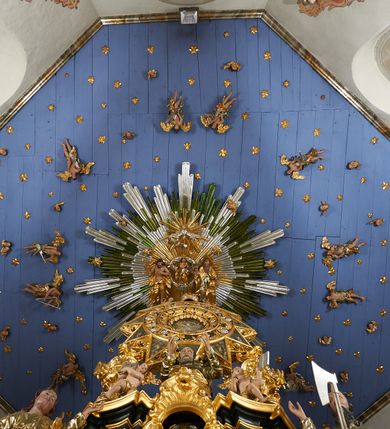 Zdjęcie nr 18: Ołtarz dwustronny, sarkofagowy, dekorowany rocaille'm, mensa drewniana na planie kwadratu, od frontu z kamiennym portatylem.
Nastawa ołtarzowa dwustronna, na rzucie leżącej litery X, w formie  rozbudowanego tabernakulum z tronem wystawienia. Obie strony są analogiczne pod względem architektonicznym. Tabernakulum na cokole, o wypukłej ściance frontowej, flankowanej parą pilastrów o trzonach dekorowanym płycinami z rocaille'm, dźwigających gzyms wieńczący. W polu drzwiczki ujęte rokokowym kartuszem. Na tabernakulum tron wystawienia o wklęsło-wypukłym licu, ujęty parą impostów podtrzymywanych przez rocaille'owe konsole oraz pilastrami w narożach, których trzony przyjmują formę spływów wolutowych, sięgające podstawy tabernakulum, na których stoją figury. W polu środkowym tronu wystawienia znajduje się obrotowa nisza o nieregularnym kształcie ujęta obramieniem z rocaille'u, przesłonięta wypukłą ścianką z płaskorzeźbionym krucyfiksem  i winnym gronem, zwieńczona rzeźbioną półpostacią. Całość wieńczy cokół z dwoma ramionami, na których stoją rocaille'owe wazony. Na cokole osadzona jest dużych rozmiarów, dwustronna, dwunastoramienna gwiazda relikwiarzowa, miażdżąca węża. Gwiazda z obu stron ujęta jest kilkoma pierścieniami z winnego grona oraz ornamentu roślinnego, w ramionach oraz w polu głównym umieszczone są za szkłem relikwie wśród kwiatowych dekoracji. 
Na awersie ołtarza, na mensie znajdują się dwie figurki puttów siedzących na obłokach i trzymających tabliczki z kanonami. Całość flankują ustawione na spływach wolutowych figury św. Jana Ewangelisty i św. Bartłomieja, tron wieńczy półpostać Boga Ojca, ujęta przez dwa putta z otwartymi księgami. Obrotową niszę flankują dwa aniołki trzymające lichtarze. Na rewersie ołtarza na spływach wolutowych stoją figury św. Andrzeja i św. Piotra, tron wieńczy półpostać Mojżesza flankowana przez dwa putta z otwartymi księgami.
Struktura polichromowana w kolorze ciemnozielonym, ornamentyka i profile złocone, detal srebrzony.
