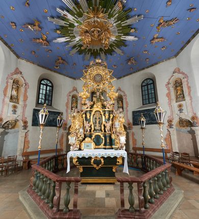 Zdjęcie nr 2: Ołtarz dwustronny, sarkofagowy, dekorowany rocaille'm, mensa drewniana na planie kwadratu, od frontu z kamiennym portatylem.
Nastawa ołtarzowa dwustronna, na rzucie leżącej litery X, w formie  rozbudowanego tabernakulum z tronem wystawienia. Obie strony są analogiczne pod względem architektonicznym. Tabernakulum na cokole, o wypukłej ściance frontowej, flankowanej parą pilastrów o trzonach dekorowanym płycinami z rocaille'm, dźwigających gzyms wieńczący. W polu drzwiczki ujęte rokokowym kartuszem. Na tabernakulum tron wystawienia o wklęsło-wypukłym licu, ujęty parą impostów podtrzymywanych przez rocaille'owe konsole oraz pilastrami w narożach, których trzony przyjmują formę spływów wolutowych, sięgające podstawy tabernakulum, na których stoją figury. W polu środkowym tronu wystawienia znajduje się obrotowa nisza o nieregularnym kształcie ujęta obramieniem z rocaille'u, przesłonięta wypukłą ścianką z płaskorzeźbionym krucyfiksem  i winnym gronem, zwieńczona rzeźbioną półpostacią. Całość wieńczy cokół z dwoma ramionami, na których stoją rocaille'owe wazony. Na cokole osadzona jest dużych rozmiarów, dwustronna, dwunastoramienna gwiazda relikwiarzowa, miażdżąca węża. Gwiazda z obu stron ujęta jest kilkoma pierścieniami z winnego grona oraz ornamentu roślinnego, w ramionach oraz w polu głównym umieszczone są za szkłem relikwie wśród kwiatowych dekoracji. 
Na awersie ołtarza, na mensie znajdują się dwie figurki puttów siedzących na obłokach i trzymających tabliczki z kanonami. Całość flankują ustawione na spływach wolutowych figury św. Jana Ewangelisty i św. Bartłomieja, tron wieńczy półpostać Boga Ojca, ujęta przez dwa putta z otwartymi księgami. Obrotową niszę flankują dwa aniołki trzymające lichtarze. Na rewersie ołtarza na spływach wolutowych stoją figury św. Andrzeja i św. Piotra, tron wieńczy półpostać Mojżesza flankowana przez dwa putta z otwartymi księgami.
Struktura polichromowana w kolorze ciemnozielonym, ornamentyka i profile złocone, detal srebrzony.
