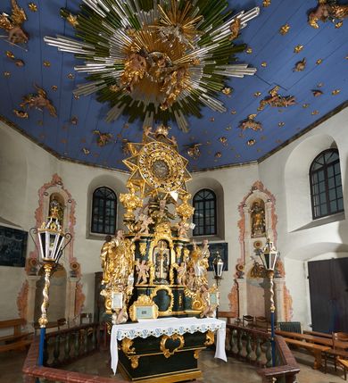 Zdjęcie nr 7: Ołtarz dwustronny, sarkofagowy, dekorowany rocaille'm, mensa drewniana na planie kwadratu, od frontu z kamiennym portatylem.
Nastawa ołtarzowa dwustronna, na rzucie leżącej litery X, w formie  rozbudowanego tabernakulum z tronem wystawienia. Obie strony są analogiczne pod względem architektonicznym. Tabernakulum na cokole, o wypukłej ściance frontowej, flankowanej parą pilastrów o trzonach dekorowanym płycinami z rocaille'm, dźwigających gzyms wieńczący. W polu drzwiczki ujęte rokokowym kartuszem. Na tabernakulum tron wystawienia o wklęsło-wypukłym licu, ujęty parą impostów podtrzymywanych przez rocaille'owe konsole oraz pilastrami w narożach, których trzony przyjmują formę spływów wolutowych, sięgające podstawy tabernakulum, na których stoją figury. W polu środkowym tronu wystawienia znajduje się obrotowa nisza o nieregularnym kształcie ujęta obramieniem z rocaille'u, przesłonięta wypukłą ścianką z płaskorzeźbionym krucyfiksem  i winnym gronem, zwieńczona rzeźbioną półpostacią. Całość wieńczy cokół z dwoma ramionami, na których stoją rocaille'owe wazony. Na cokole osadzona jest dużych rozmiarów, dwustronna, dwunastoramienna gwiazda relikwiarzowa, miażdżąca węża. Gwiazda z obu stron ujęta jest kilkoma pierścieniami z winnego grona oraz ornamentu roślinnego, w ramionach oraz w polu głównym umieszczone są za szkłem relikwie wśród kwiatowych dekoracji. 
Na awersie ołtarza, na mensie znajdują się dwie figurki puttów siedzących na obłokach i trzymających tabliczki z kanonami. Całość flankują ustawione na spływach wolutowych figury św. Jana Ewangelisty i św. Bartłomieja, tron wieńczy półpostać Boga Ojca, ujęta przez dwa putta z otwartymi księgami. Obrotową niszę flankują dwa aniołki trzymające lichtarze. Na rewersie ołtarza na spływach wolutowych stoją figury św. Andrzeja i św. Piotra, tron wieńczy półpostać Mojżesza flankowana przez dwa putta z otwartymi księgami.
Struktura polichromowana w kolorze ciemnozielonym, ornamentyka i profile złocone, detal srebrzony.
