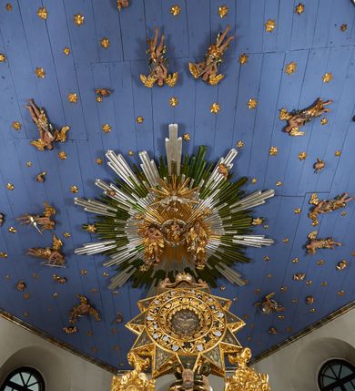 Zdjęcie nr 19: Ołtarz dwustronny, sarkofagowy, dekorowany rocaille'm, mensa drewniana na planie kwadratu, od frontu z kamiennym portatylem.
Nastawa ołtarzowa dwustronna, na rzucie leżącej litery X, w formie  rozbudowanego tabernakulum z tronem wystawienia. Obie strony są analogiczne pod względem architektonicznym. Tabernakulum na cokole, o wypukłej ściance frontowej, flankowanej parą pilastrów o trzonach dekorowanym płycinami z rocaille'm, dźwigających gzyms wieńczący. W polu drzwiczki ujęte rokokowym kartuszem. Na tabernakulum tron wystawienia o wklęsło-wypukłym licu, ujęty parą impostów podtrzymywanych przez rocaille'owe konsole oraz pilastrami w narożach, których trzony przyjmują formę spływów wolutowych, sięgające podstawy tabernakulum, na których stoją figury. W polu środkowym tronu wystawienia znajduje się obrotowa nisza o nieregularnym kształcie ujęta obramieniem z rocaille'u, przesłonięta wypukłą ścianką z płaskorzeźbionym krucyfiksem  i winnym gronem, zwieńczona rzeźbioną półpostacią. Całość wieńczy cokół z dwoma ramionami, na których stoją rocaille'owe wazony. Na cokole osadzona jest dużych rozmiarów, dwustronna, dwunastoramienna gwiazda relikwiarzowa, miażdżąca węża. Gwiazda z obu stron ujęta jest kilkoma pierścieniami z winnego grona oraz ornamentu roślinnego, w ramionach oraz w polu głównym umieszczone są za szkłem relikwie wśród kwiatowych dekoracji. 
Na awersie ołtarza, na mensie znajdują się dwie figurki puttów siedzących na obłokach i trzymających tabliczki z kanonami. Całość flankują ustawione na spływach wolutowych figury św. Jana Ewangelisty i św. Bartłomieja, tron wieńczy półpostać Boga Ojca, ujęta przez dwa putta z otwartymi księgami. Obrotową niszę flankują dwa aniołki trzymające lichtarze. Na rewersie ołtarza na spływach wolutowych stoją figury św. Andrzeja i św. Piotra, tron wieńczy półpostać Mojżesza flankowana przez dwa putta z otwartymi księgami.
Struktura polichromowana w kolorze ciemnozielonym, ornamentyka i profile złocone, detal srebrzony.
