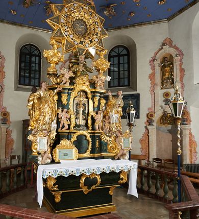 Zdjęcie nr 9: Ołtarz dwustronny, sarkofagowy, dekorowany rocaille'm, mensa drewniana na planie kwadratu, od frontu z kamiennym portatylem.
Nastawa ołtarzowa dwustronna, na rzucie leżącej litery X, w formie  rozbudowanego tabernakulum z tronem wystawienia. Obie strony są analogiczne pod względem architektonicznym. Tabernakulum na cokole, o wypukłej ściance frontowej, flankowanej parą pilastrów o trzonach dekorowanym płycinami z rocaille'm, dźwigających gzyms wieńczący. W polu drzwiczki ujęte rokokowym kartuszem. Na tabernakulum tron wystawienia o wklęsło-wypukłym licu, ujęty parą impostów podtrzymywanych przez rocaille'owe konsole oraz pilastrami w narożach, których trzony przyjmują formę spływów wolutowych, sięgające podstawy tabernakulum, na których stoją figury. W polu środkowym tronu wystawienia znajduje się obrotowa nisza o nieregularnym kształcie ujęta obramieniem z rocaille'u, przesłonięta wypukłą ścianką z płaskorzeźbionym krucyfiksem  i winnym gronem, zwieńczona rzeźbioną półpostacią. Całość wieńczy cokół z dwoma ramionami, na których stoją rocaille'owe wazony. Na cokole osadzona jest dużych rozmiarów, dwustronna, dwunastoramienna gwiazda relikwiarzowa, miażdżąca węża. Gwiazda z obu stron ujęta jest kilkoma pierścieniami z winnego grona oraz ornamentu roślinnego, w ramionach oraz w polu głównym umieszczone są za szkłem relikwie wśród kwiatowych dekoracji. 
Na awersie ołtarza, na mensie znajdują się dwie figurki puttów siedzących na obłokach i trzymających tabliczki z kanonami. Całość flankują ustawione na spływach wolutowych figury św. Jana Ewangelisty i św. Bartłomieja, tron wieńczy półpostać Boga Ojca, ujęta przez dwa putta z otwartymi księgami. Obrotową niszę flankują dwa aniołki trzymające lichtarze. Na rewersie ołtarza na spływach wolutowych stoją figury św. Andrzeja i św. Piotra, tron wieńczy półpostać Mojżesza flankowana przez dwa putta z otwartymi księgami.
Struktura polichromowana w kolorze ciemnozielonym, ornamentyka i profile złocone, detal srebrzony.
