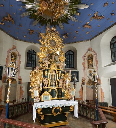 Zdjęcie nr 8: Ołtarz dwustronny, sarkofagowy, dekorowany rocaille'm, mensa drewniana na planie kwadratu, od frontu z kamiennym portatylem.
Nastawa ołtarzowa dwustronna, na rzucie leżącej litery X, w formie  rozbudowanego tabernakulum z tronem wystawienia. Obie strony są analogiczne pod względem architektonicznym. Tabernakulum na cokole, o wypukłej ściance frontowej, flankowanej parą pilastrów o trzonach dekorowanym płycinami z rocaille'm, dźwigających gzyms wieńczący. W polu drzwiczki ujęte rokokowym kartuszem. Na tabernakulum tron wystawienia o wklęsło-wypukłym licu, ujęty parą impostów podtrzymywanych przez rocaille'owe konsole oraz pilastrami w narożach, których trzony przyjmują formę spływów wolutowych, sięgające podstawy tabernakulum, na których stoją figury. W polu środkowym tronu wystawienia znajduje się obrotowa nisza o nieregularnym kształcie ujęta obramieniem z rocaille'u, przesłonięta wypukłą ścianką z płaskorzeźbionym krucyfiksem  i winnym gronem, zwieńczona rzeźbioną półpostacią. Całość wieńczy cokół z dwoma ramionami, na których stoją rocaille'owe wazony. Na cokole osadzona jest dużych rozmiarów, dwustronna, dwunastoramienna gwiazda relikwiarzowa, miażdżąca węża. Gwiazda z obu stron ujęta jest kilkoma pierścieniami z winnego grona oraz ornamentu roślinnego, w ramionach oraz w polu głównym umieszczone są za szkłem relikwie wśród kwiatowych dekoracji. 
Na awersie ołtarza, na mensie znajdują się dwie figurki puttów siedzących na obłokach i trzymających tabliczki z kanonami. Całość flankują ustawione na spływach wolutowych figury św. Jana Ewangelisty i św. Bartłomieja, tron wieńczy półpostać Boga Ojca, ujęta przez dwa putta z otwartymi księgami. Obrotową niszę flankują dwa aniołki trzymające lichtarze. Na rewersie ołtarza na spływach wolutowych stoją figury św. Andrzeja i św. Piotra, tron wieńczy półpostać Mojżesza flankowana przez dwa putta z otwartymi księgami.
Struktura polichromowana w kolorze ciemnozielonym, ornamentyka i profile złocone, detal srebrzony.
