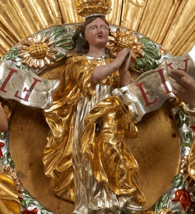 Zdjęcie nr 46: Ołtarz dwustronny, sarkofagowy, dekorowany rocaille&#039;m, mensa drewniana na planie kwadratu, od frontu z kamiennym portatylem.
Nastawa ołtarzowa dwustronna, na rzucie leżącej litery X, w formie  rozbudowanego tabernakulum z tronem wystawienia. Obie strony są analogiczne pod względem architektonicznym. Tabernakulum na cokole, o wypukłej ściance frontowej, flankowanej parą pilastrów o trzonach dekorowanym płycinami z rocaille&#039;m, dźwigających gzyms wieńczący. W polu drzwiczki ujęte rokokowym kartuszem. Na tabernakulum tron wystawienia o wklęsło-wypukłym licu, ujęty parą impostów podtrzymywanych przez rocaille&#039;owe konsole oraz pilastrami w narożach, których trzony przyjmują formę spływów wolutowych, sięgające podstawy tabernakulum, na których stoją figury. W polu środkowym tronu wystawienia znajduje się obrotowa nisza o nieregularnym kształcie ujęta obramieniem z rocaille&#039;u, przesłonięta wypukłą ścianką z płaskorzeźbionym krucyfiksem  i winnym gronem, zwieńczona rzeźbioną półpostacią. Całość wieńczy cokół z dwoma ramionami, na których stoją rocaille&#039;owe wazony. Na cokole osadzona jest dużych rozmiarów, dwustronna, dwunastoramienna gwiazda relikwiarzowa, miażdżąca węża. Gwiazda z obu stron ujęta jest kilkoma pierścieniami z winnego grona oraz ornamentu roślinnego, w ramionach oraz w polu głównym umieszczone są za szkłem relikwie wśród kwiatowych dekoracji. 
Na awersie ołtarza, na mensie znajdują się dwie figurki puttów siedzących na obłokach i trzymających tabliczki z kanonami. Całość flankują ustawione na spływach wolutowych figury św. Jana Ewangelisty i św. Bartłomieja, tron wieńczy półpostać Boga Ojca, ujęta przez dwa putta z otwartymi księgami. Obrotową niszę flankują dwa aniołki trzymające lichtarze. Na rewersie ołtarza na spływach wolutowych stoją figury św. Andrzeja i św. Piotra, tron wieńczy półpostać Mojżesza flankowana przez dwa putta z otwartymi księgami.
Struktura polichromowana w kolorze ciemnozielonym, ornamentyka i profile złocone, detal srebrzony.
