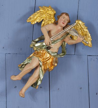 Zdjęcie nr 5: Drewniany, polichromowany na niebiesko strop, na planie ośmioboku, ujęty profilowaną ramą. W jego centrum grupa Koronacji Marii w glorii promienistej. W środku grupy figura Matki Boskiej na tle opaski dekorowanej kwiatami. Maria ukazana frontalnie, w kontrapoście, z rękami złożonymi w geście modlitwy. Twarz ma pociągłą, szczupłą, o młodzieńczych rysach, okoloną długimi włosami, upiętymi z tyłu głowy. Ubrana jest w srebrzoną suknię oraz złocony płaszcz narzucony na ramiona i zawinięty na lewej nodze, na głowie ma koronę zamkniętą. Marię flankują dwie banderole z napisem: „FIAT”. Po jej prawej znacznie większa figura Chrystusa, ukazanego frontalnie, w pozycji siedzącej, z głową skierowaną do wewnątrz; jego lewa ręka spoczywa na piersi, prawa jest ugięta i uniesiona w geście wskazującym. Twarz ma pociągłą, szczupłą, okoloną brodą skręconą w dwa pukle, oraz kręconymi włosami. Chrystus przewiązany jest w partii bioder złoconym płaszczem otaczającym postać i odsłaniającym lewą nogę. Jego ciało w odsłoniętych partiach, ma delikatnie zarysowaną muskulaturę, z zaznaczonymi śladami męki. Po lewej stronie Marii znacznie większa figura Boga Ojca, ukazanego frontalnie, w pozycji siedzącej. Lewą ręką przytrzymuje jabłko królewskie, w dłoni dzierży berło, prawą wyciąga w geście błogosławieństwa. Twarz ma pociągłą, o starczych rysach, okoloną długą, kręconą brodą opadającą na pierś oraz krótkimi włosami. Ubrany jest w obficie drapowaną srebrzoną tunikę, przepasaną w talii oraz złocony płaszcz z dekoracyjną, kameryzowaną lamówką, zapięty na piersi i opadający na boki, z zawiniętym fragmentem tkaniny na lewej nodze. Nad postaciami nadlatująca gołębica Ducha Świętego w glorii promienistej z banderolą z napisem: „FIAT”. Grupa na tle trzystrefowej glorii promienistej dekorowanej gwiazdami i uskrzydlonymi główkami anielskimi. Glorię z grupą Koronacji otacza dwunastu aniołów, ułożonych naprzemiennie w cztery pary muzykujących postaci (ze skrzypcami, wiolonczelą, gitarą, trąbką, harfą) z czterema aniołami podtrzymującymi tace z symbolicznymi przedmiotami (różaniec, wieniec laurowy, chleb (?), dyscyplina). Strop dekorowany jest w całości gwiazdami i uskrzydlonymi główkami anielskimi. Figury w partiach ciała polichromowane są naturalistycznie, ich szaty są złocone, srebrzone i laserowane; atrybuty są srebrzone. 

